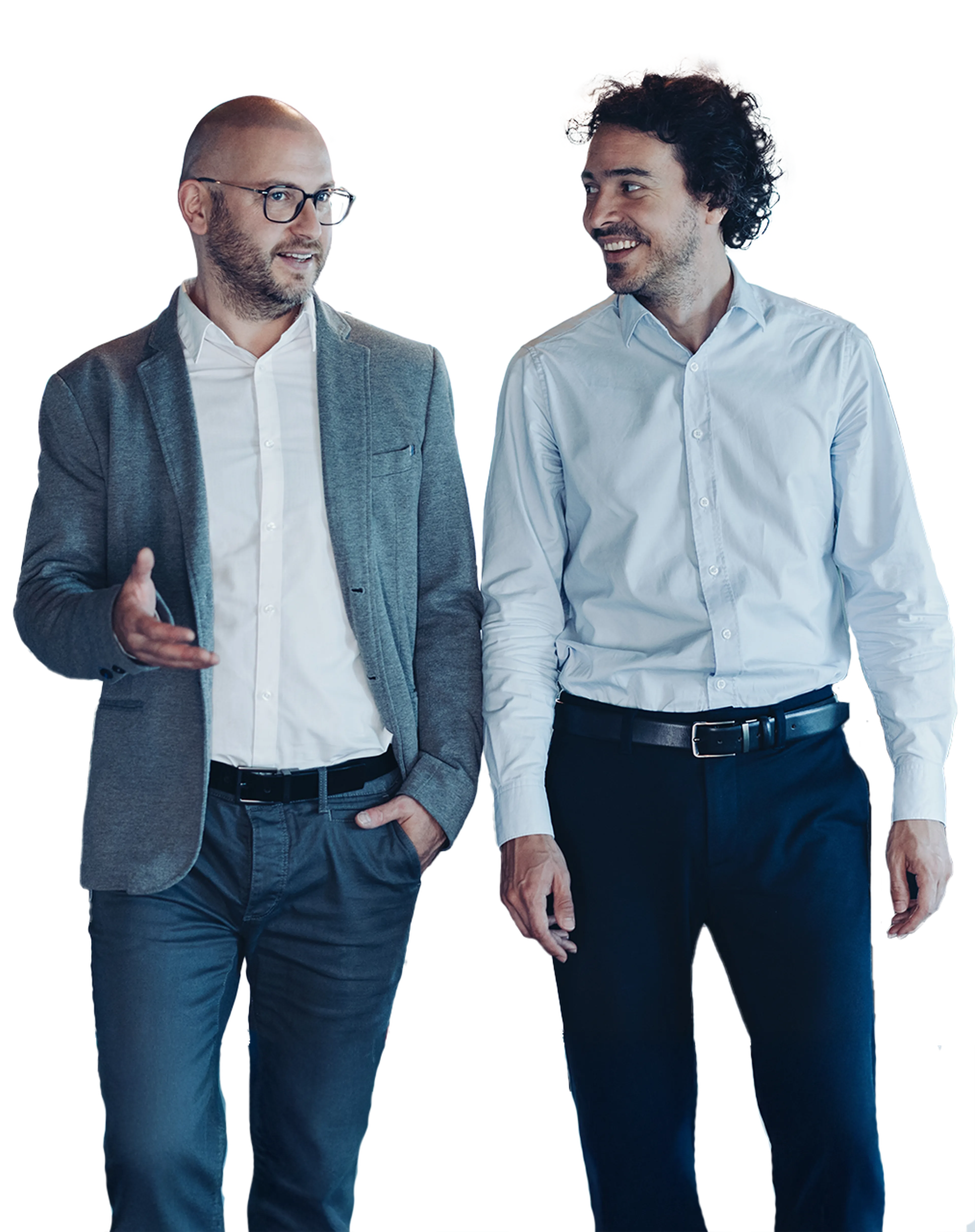 Two men walking and talking, one in a gray blazer and glasses, the other in a light blue shirt. Both appear engaged in conversation.