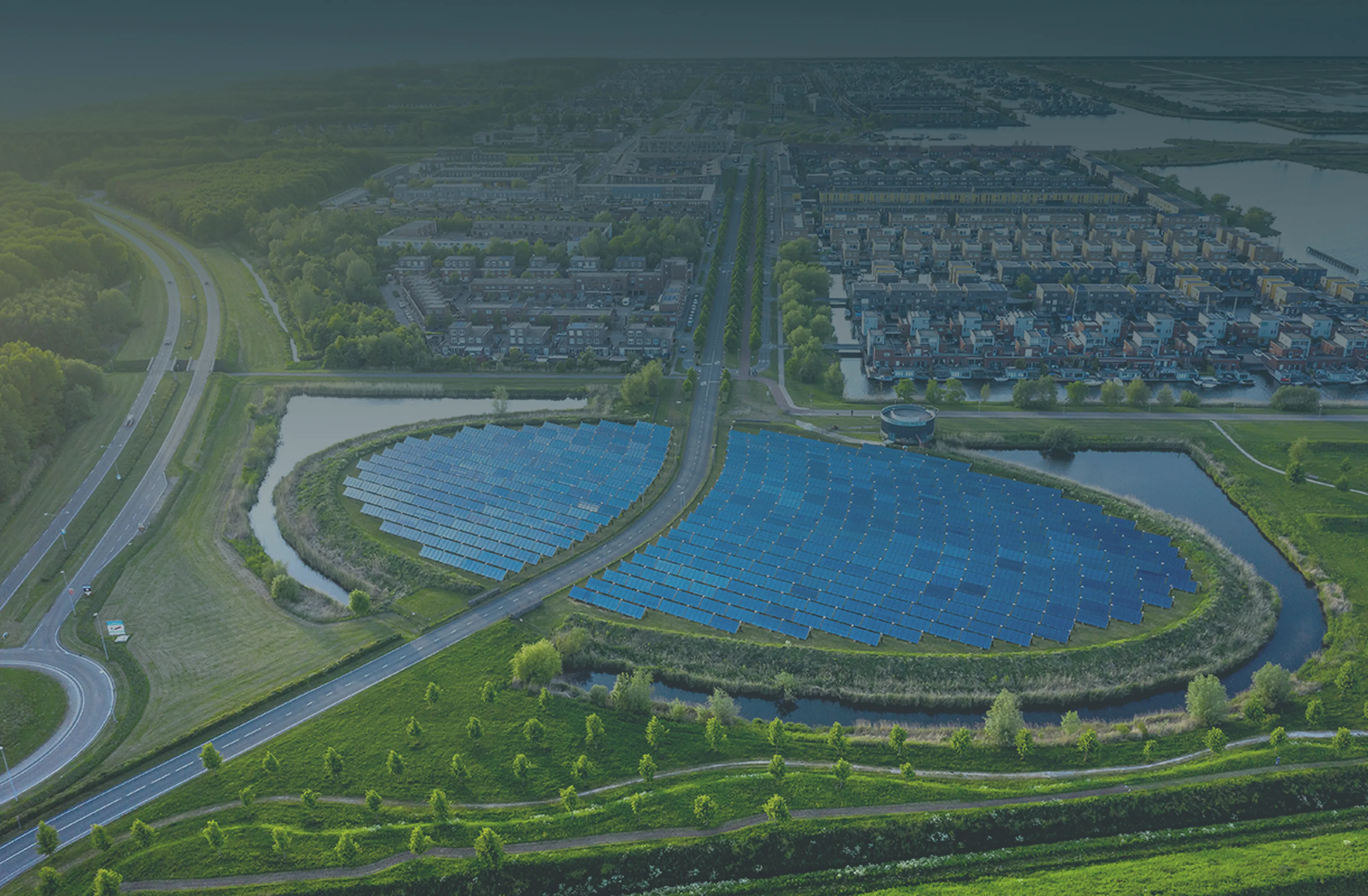Aerial view of a solar panel array near a residential area, surrounded by greenery and intersected by roads, under a clear sky.