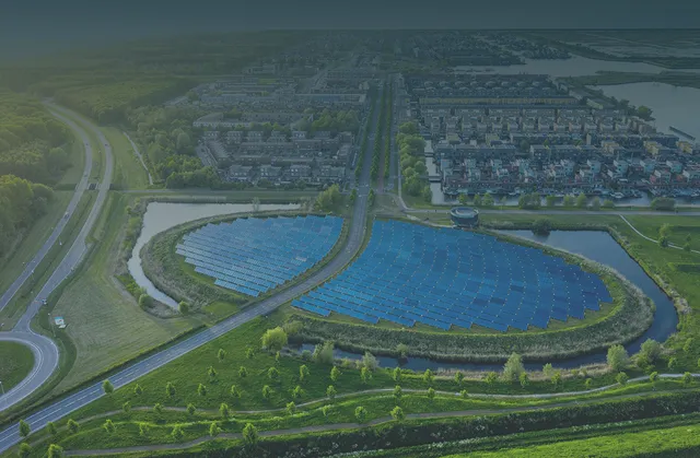 Aerial view of a solar panel array near a residential area, surrounded by greenery and intersected by roads, under a clear sky.