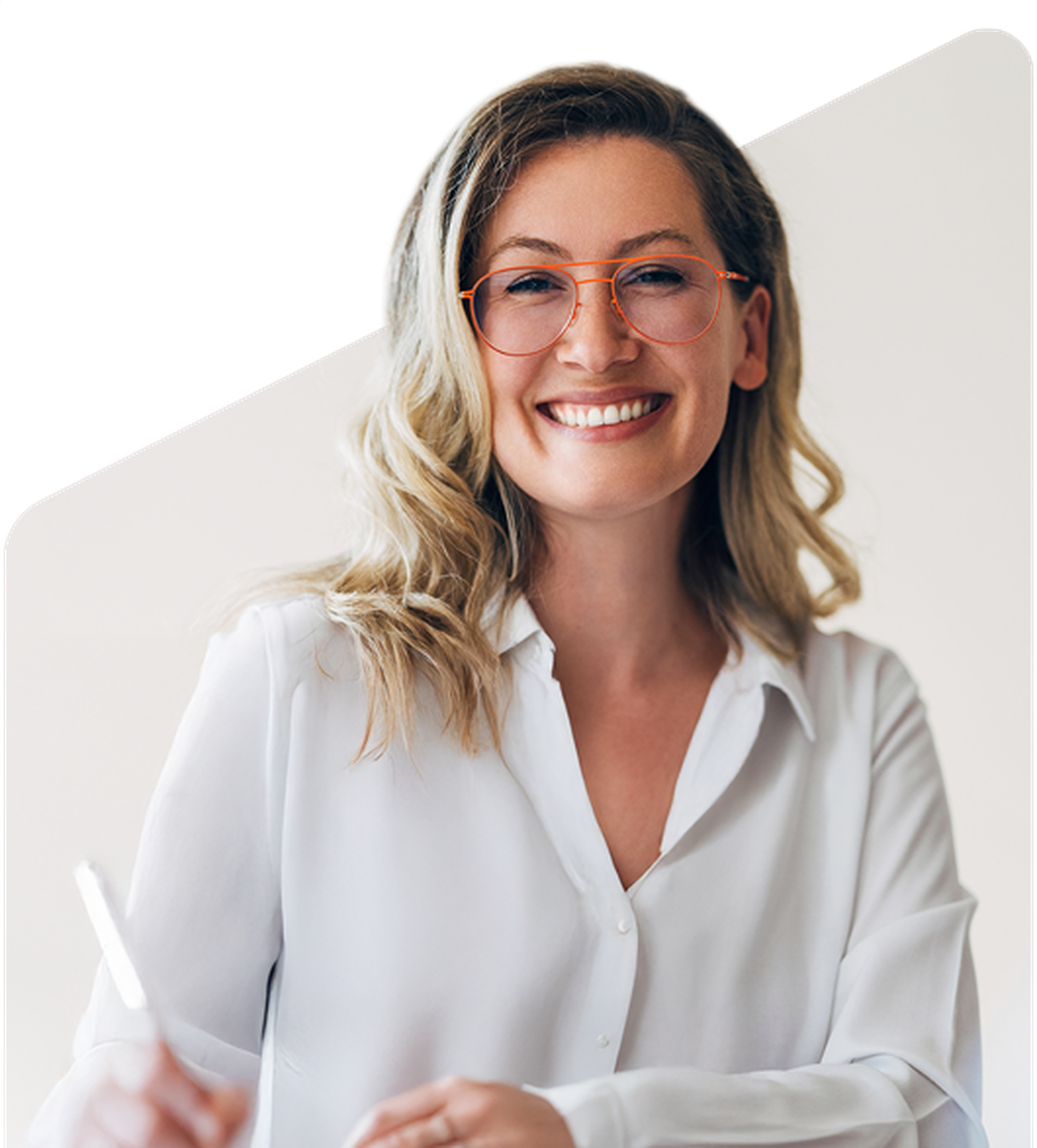 Smiling woman with wavy blonde hair and glasses, wearing a white blouse, holding a pen against a plain background.