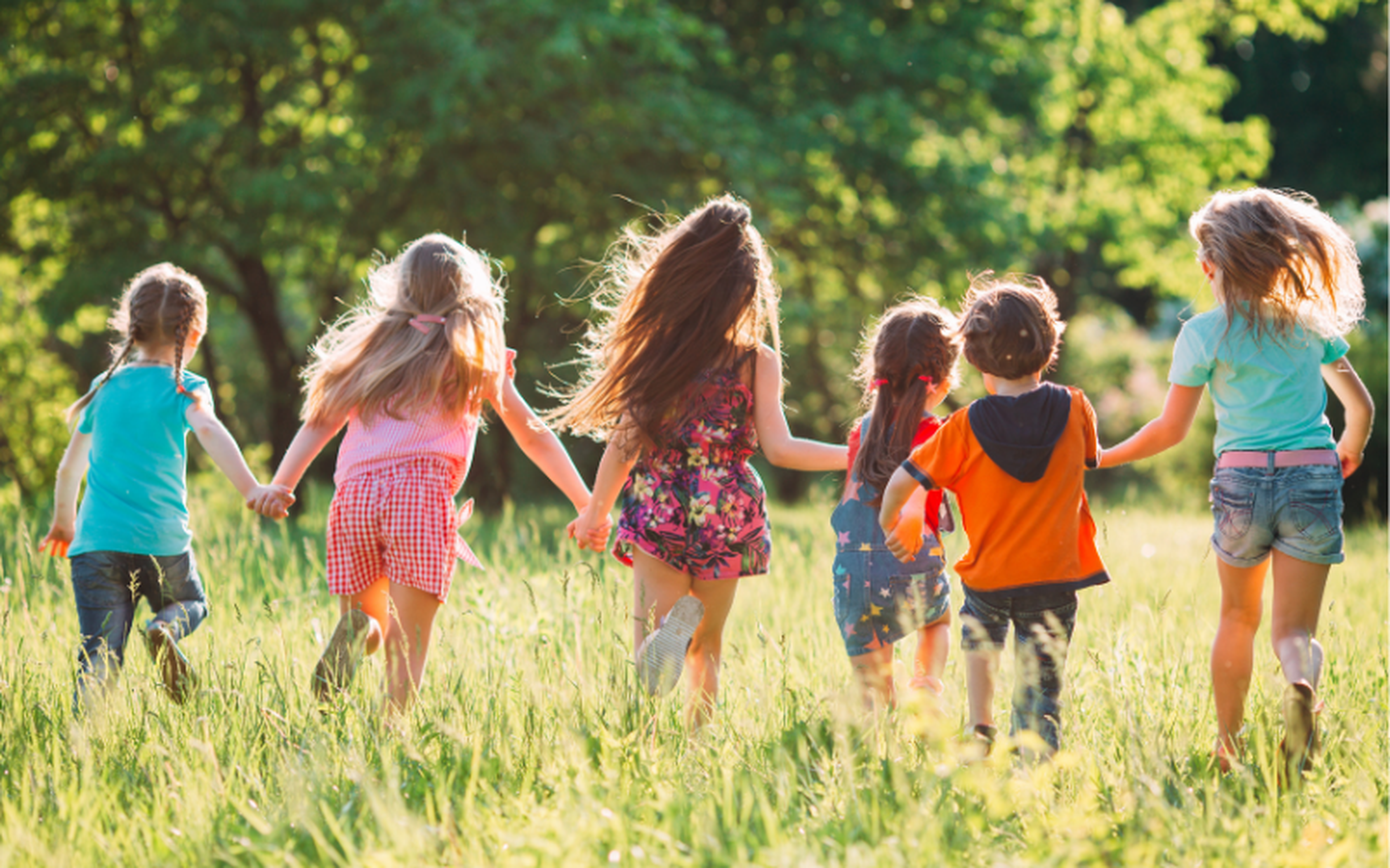 Large group of children running together through a park on a sunny summer day.