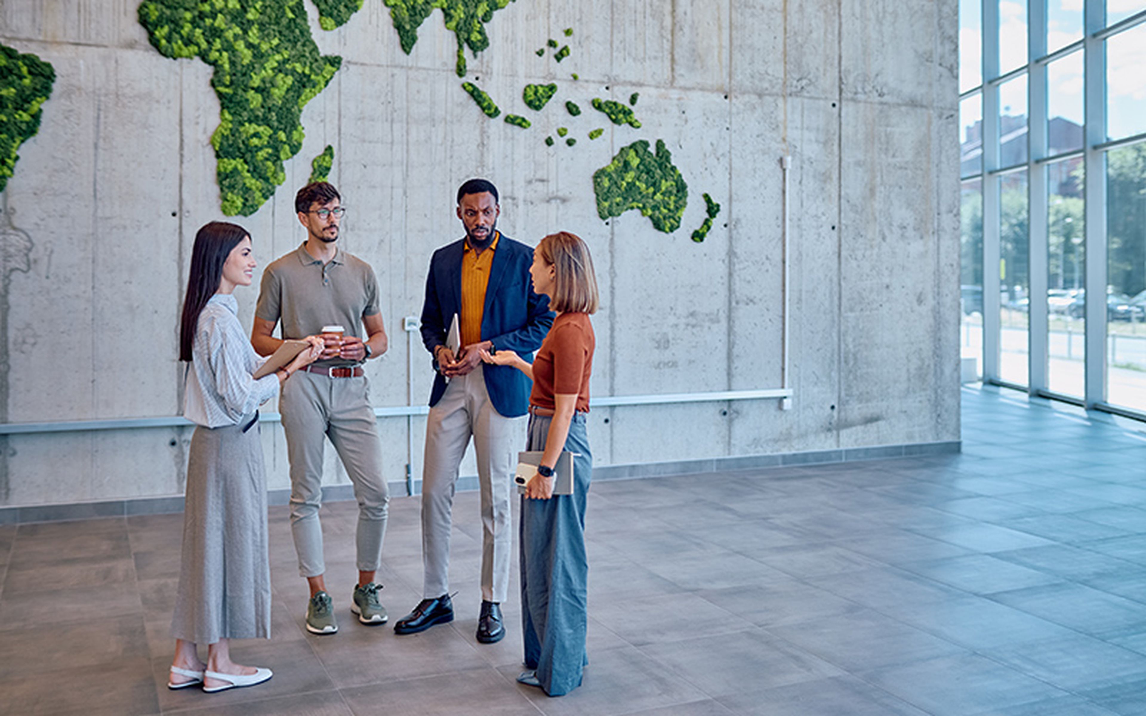 Four colleagues discussing in a modern office with a vertical garden wall shaped like a world map.