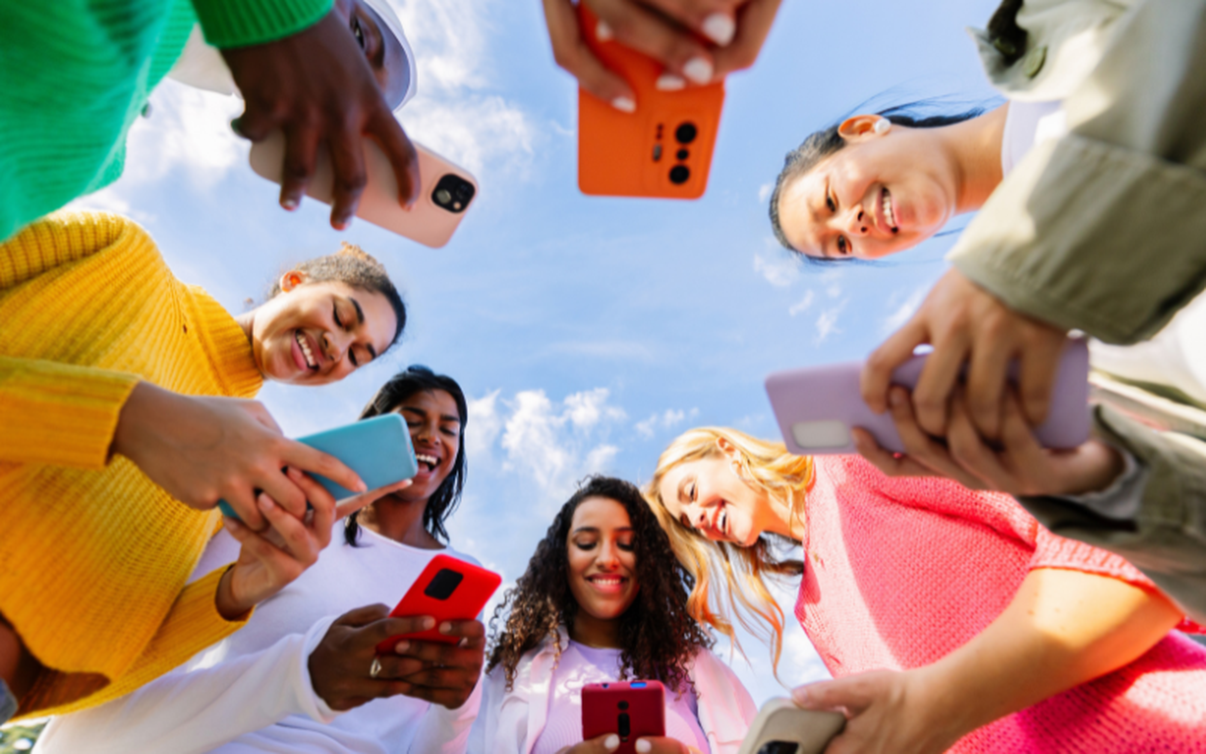 Young women from diverse backgrounds looking at their mobile phones while socializing in an urban setting.