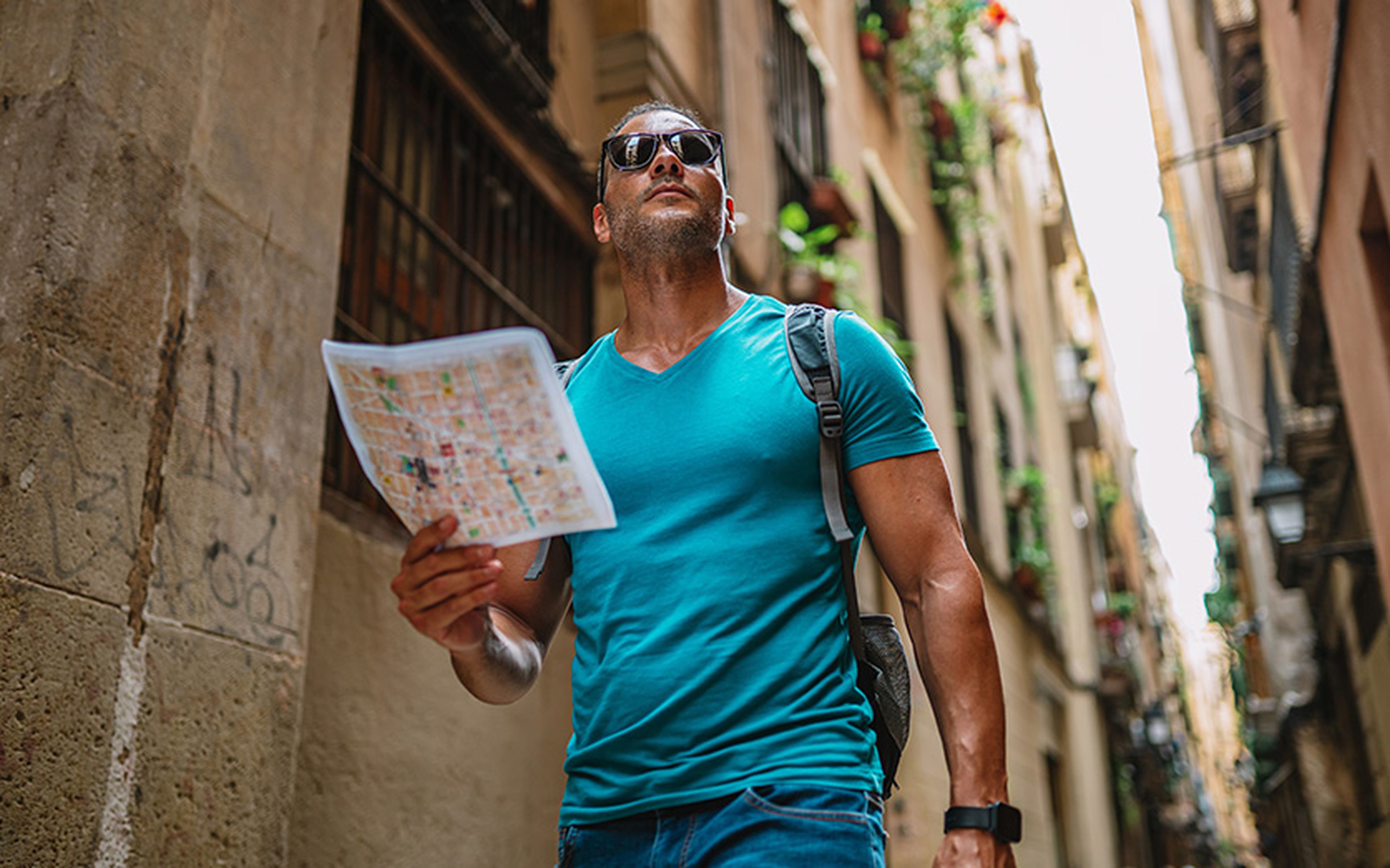 Smiling male tourist navigating a narrow alley in Barcelona’s old town while holding a paper map.