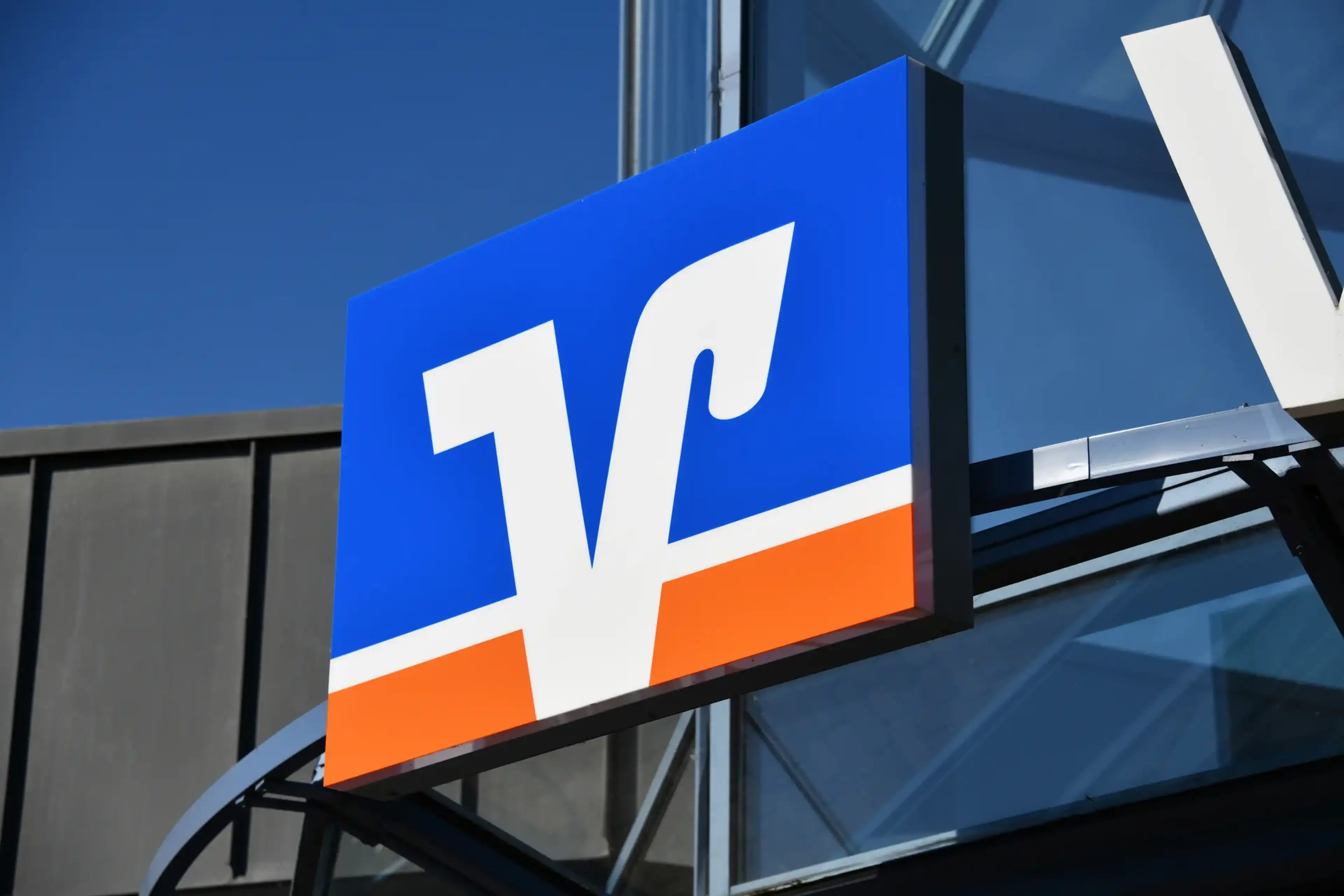 Blue and orange sign with a white logo on a building exterior, set against a clear blue sky.