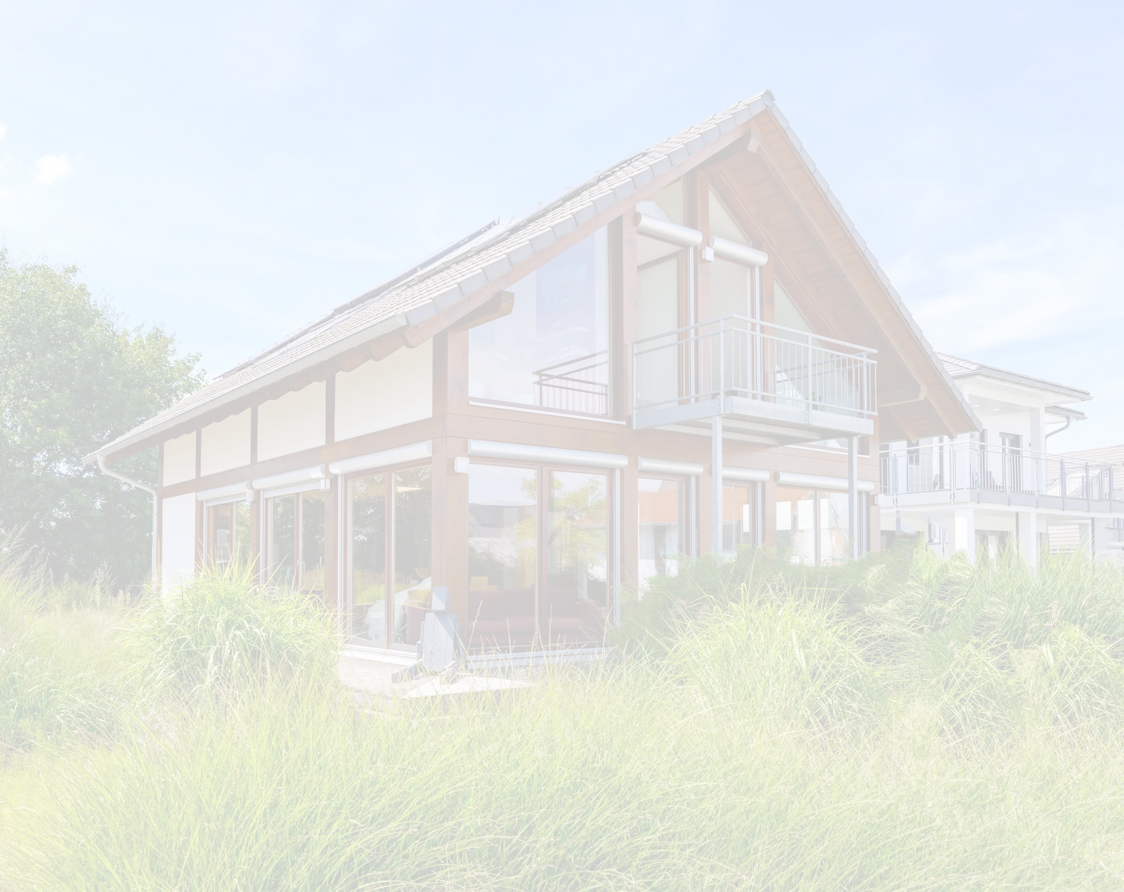 Modern house with large glass windows, wooden accents, and a balcony, surrounded by lush green grass under a clear blue sky.