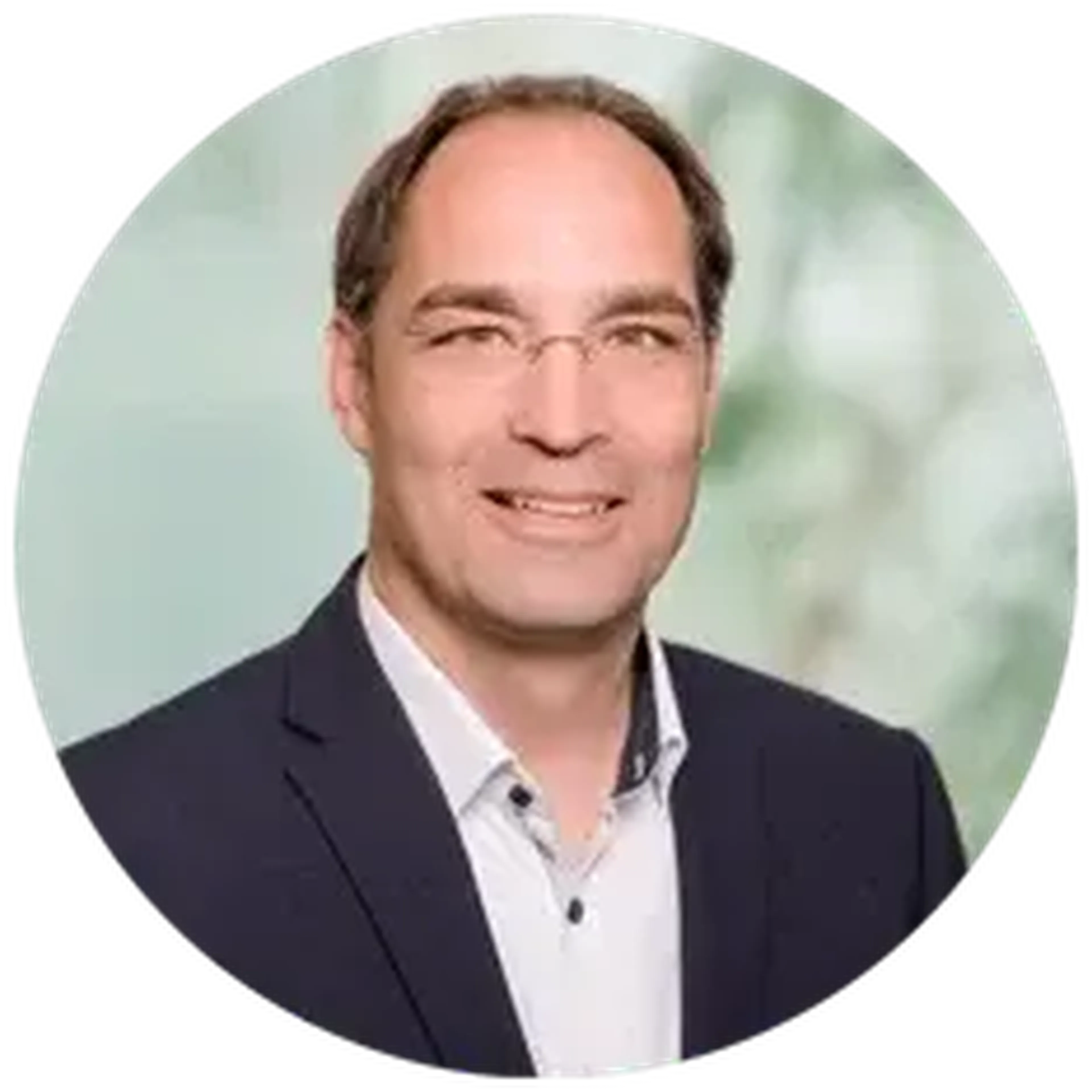 A man in a suit and white shirt smiles against a blurred background.