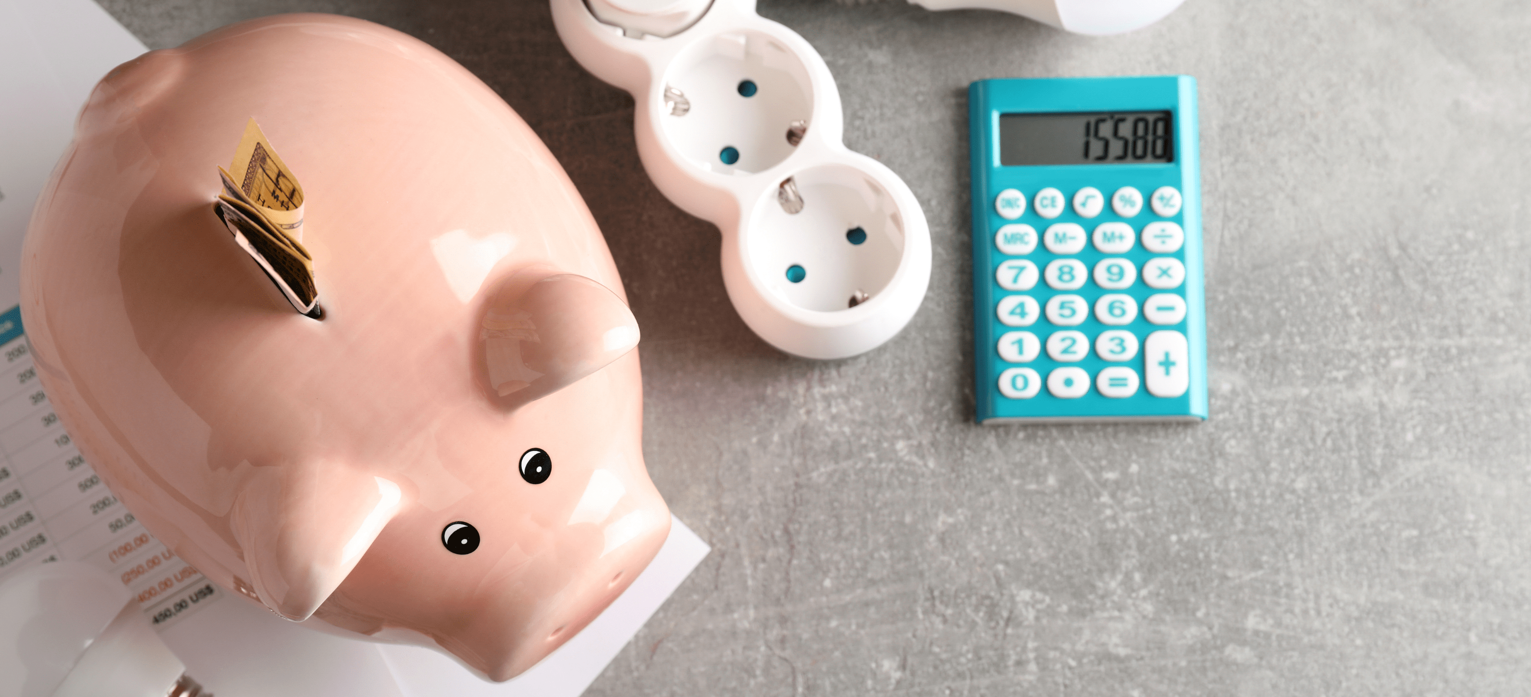 Ein Sparschwein, Taschenrechner und ein paar Glühbirnen auf einem Tisch