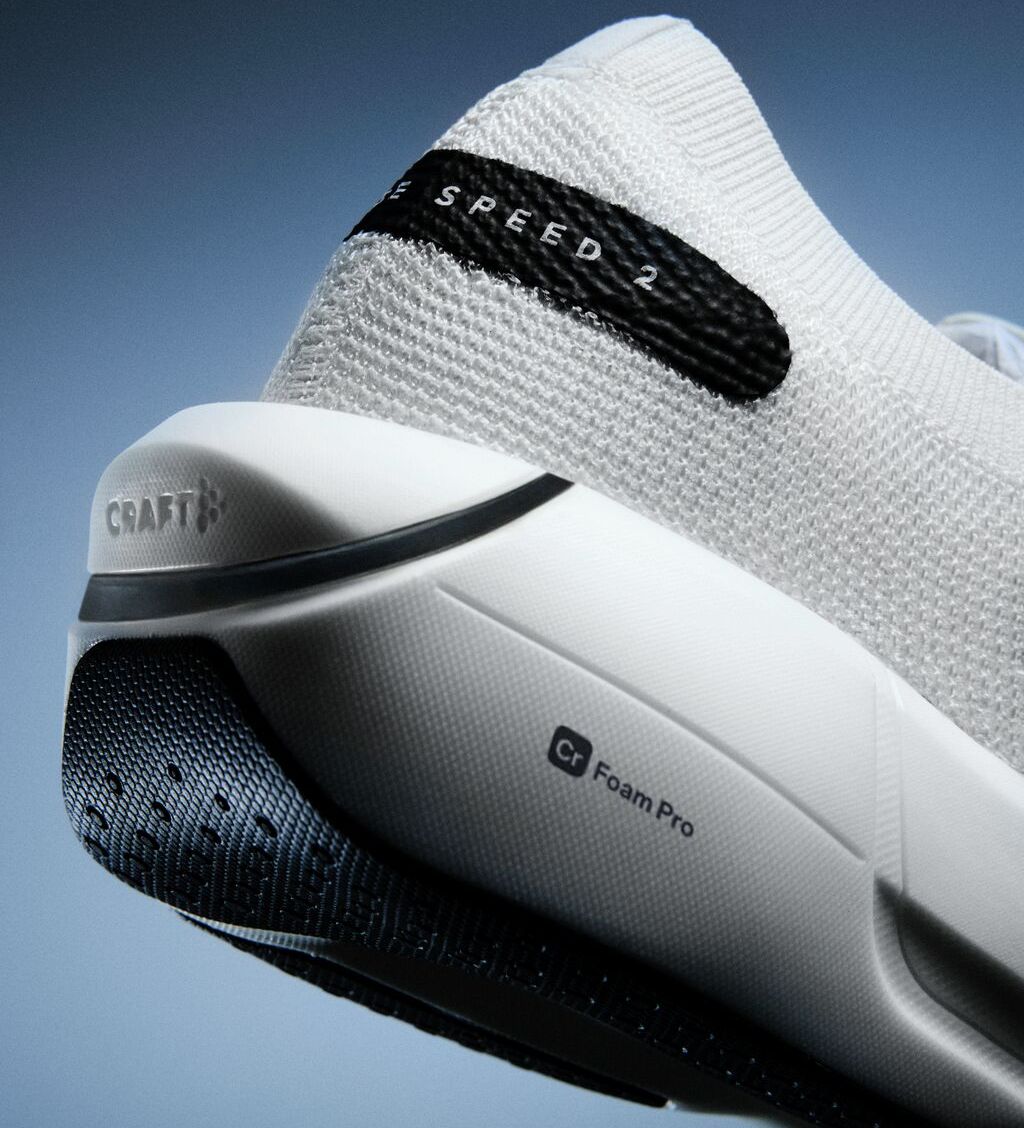 Nærbilde av en hvit joggesko med teksten «Speed 2» og «Cr Foam Pro»-teknologi, som viser en strukturert såle og hæl mot en blå bakgrunn.