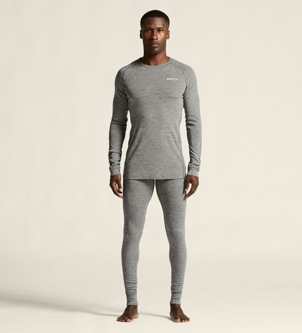 Person som står barbeint og har på seg grå langermet superundertøy-topp og leggings mot en ensfarget bakgrunn.