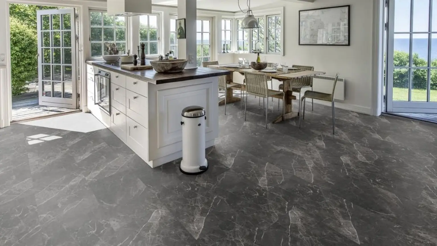 Bright kitchen with gray marble-pattern flooring, white cabinetry, and garden views.