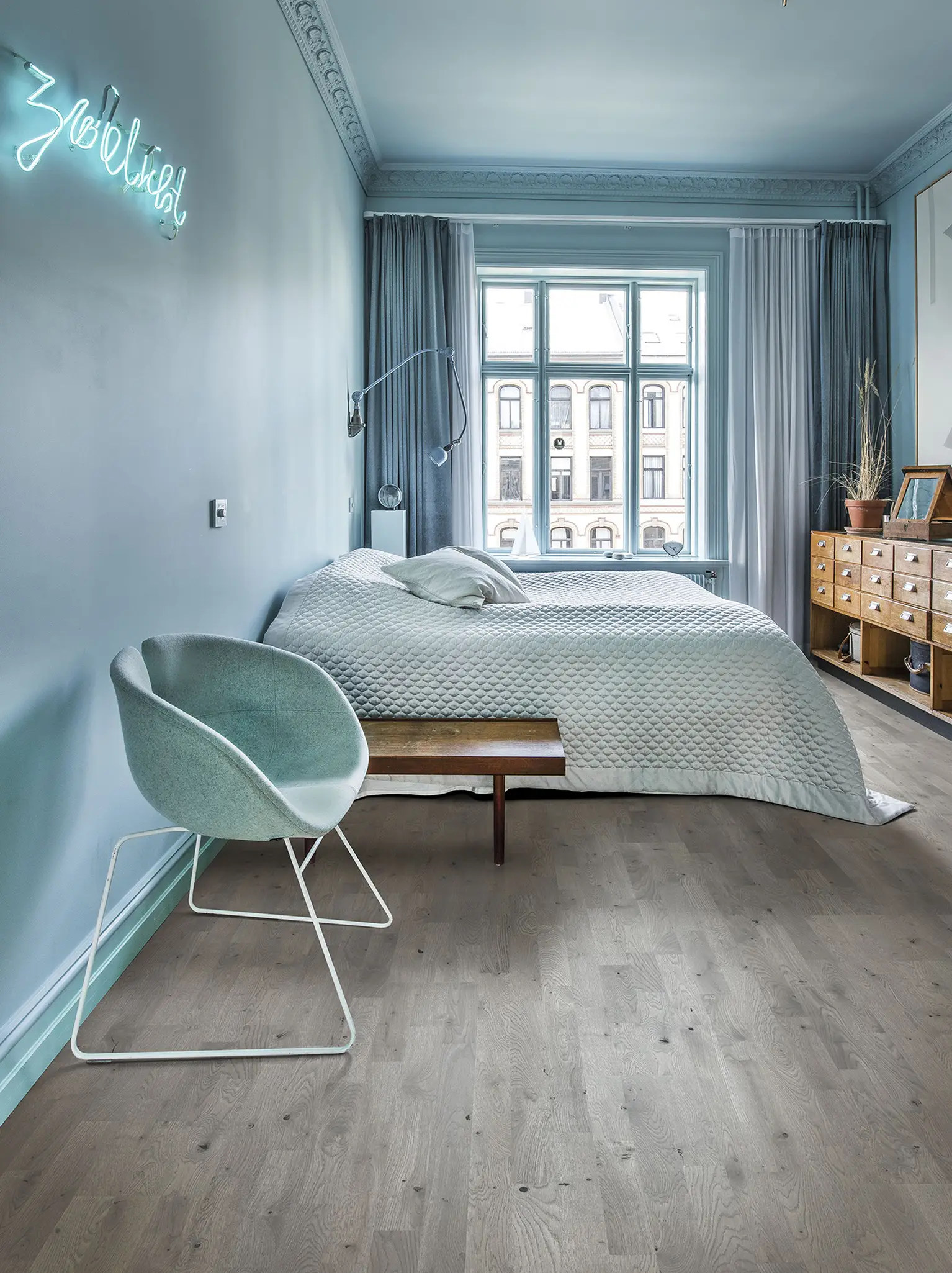 Minimalist blue bedroom with gwood floors and large windows overlooking a city.