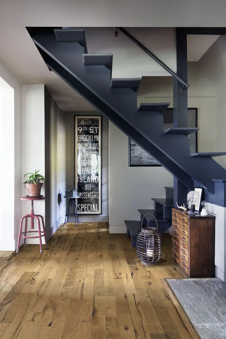 Oak Decorum. An industrial-style entryway with rustic oak flooring, a dark staircase, and vintage decor.