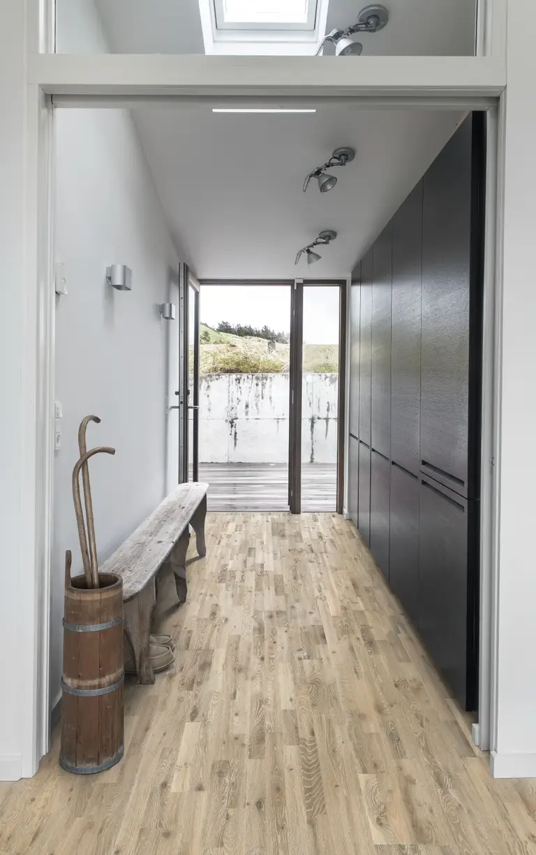 Oak Kilesand. A bright entryway with light oak flooring, a rustic wooden bench, and modern black cabinetry.