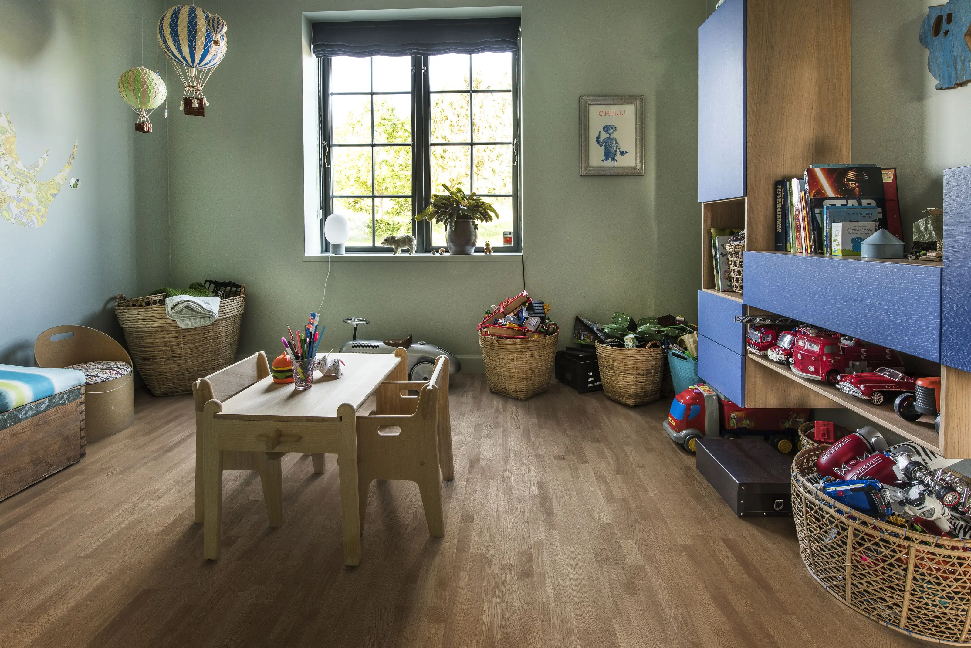 A cheerful playroom with light wooden flooring, colorful toys, storage baskets, and whimsical hot air balloon decorations.