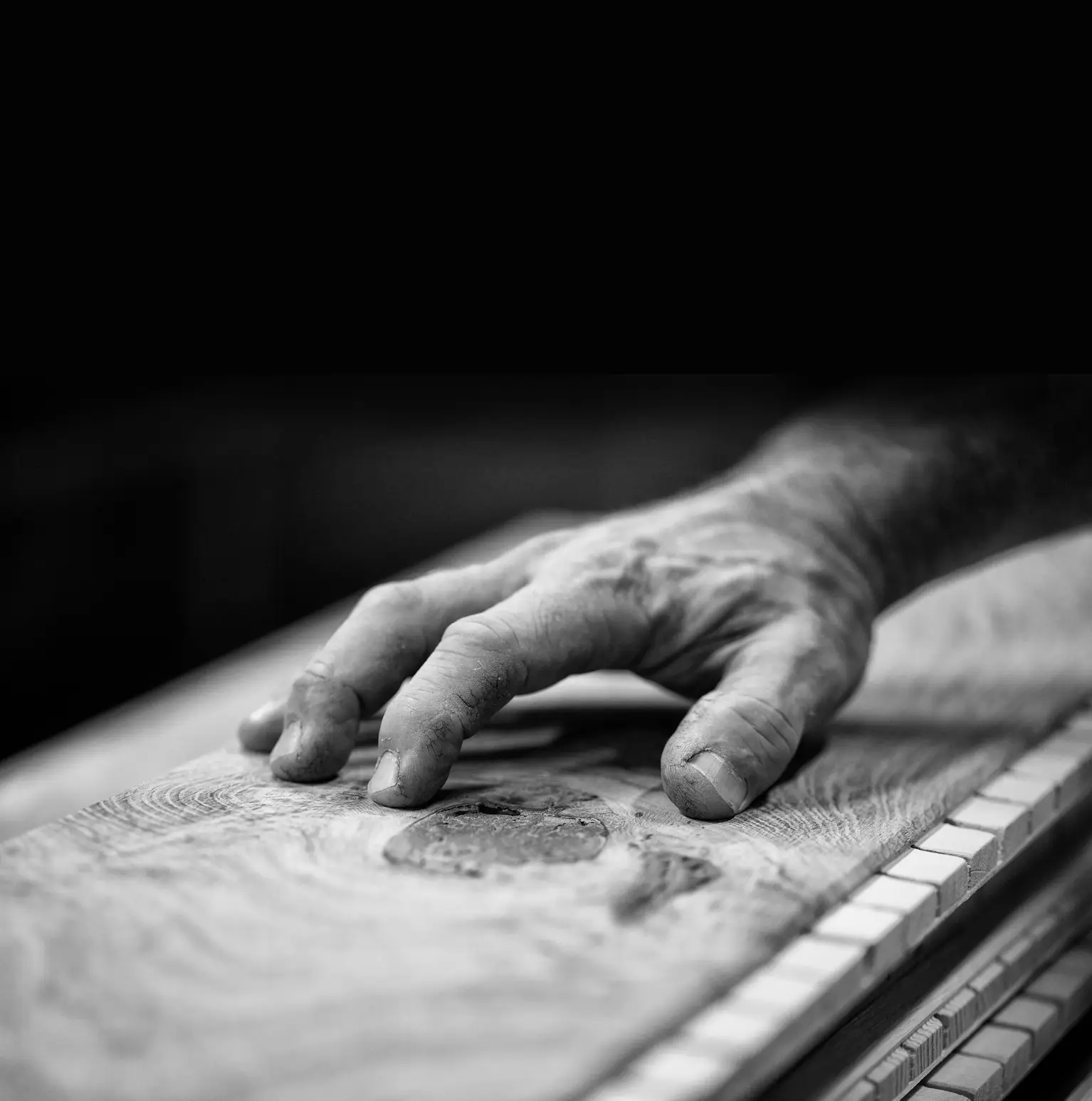 A black and white image of an artisan’s hand running over a wooden surface, showcasing craftsmanship and texture.