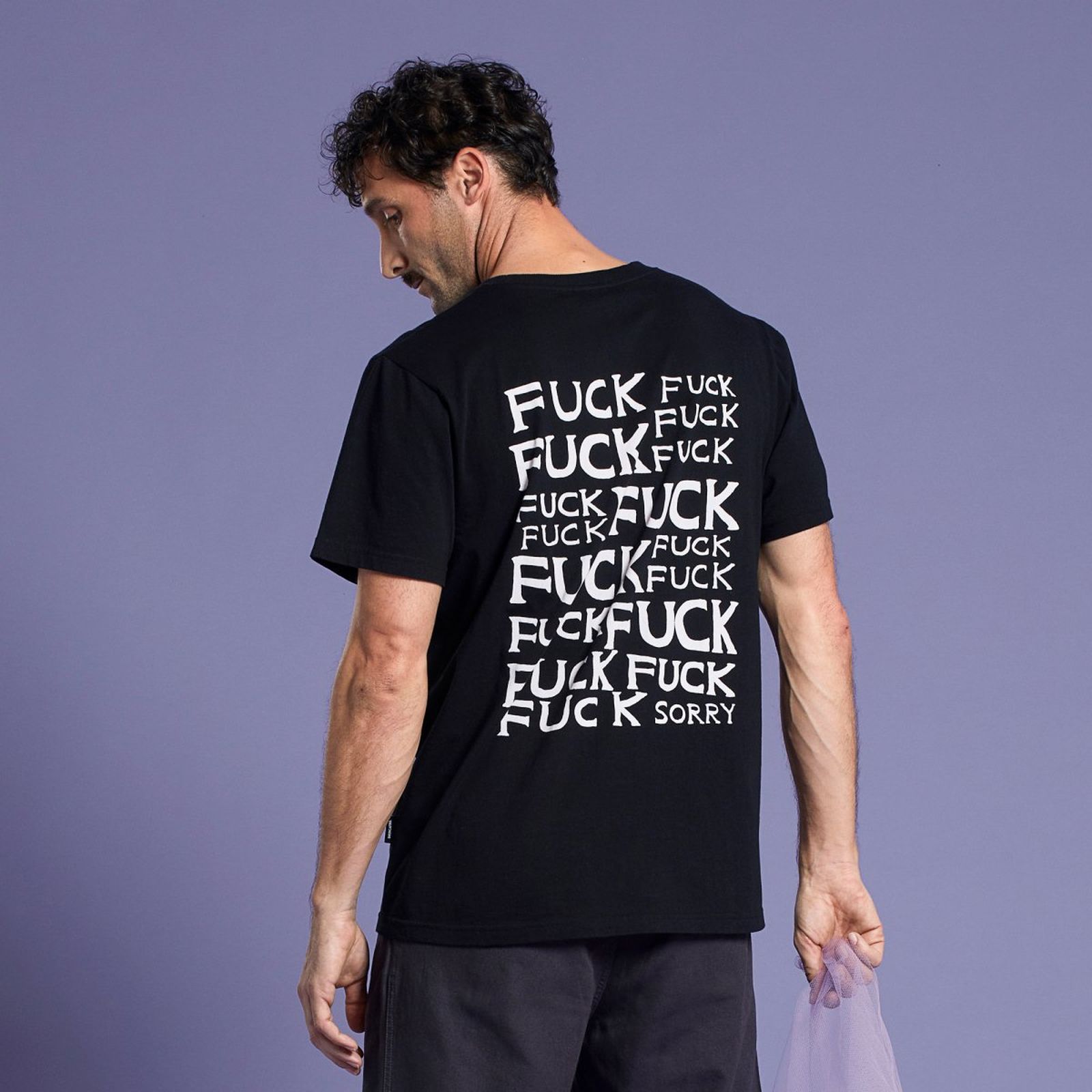 Man in a black T-shirt with repeated "FUCK" text and "SORRY" at the bottom, standing against a purple background.