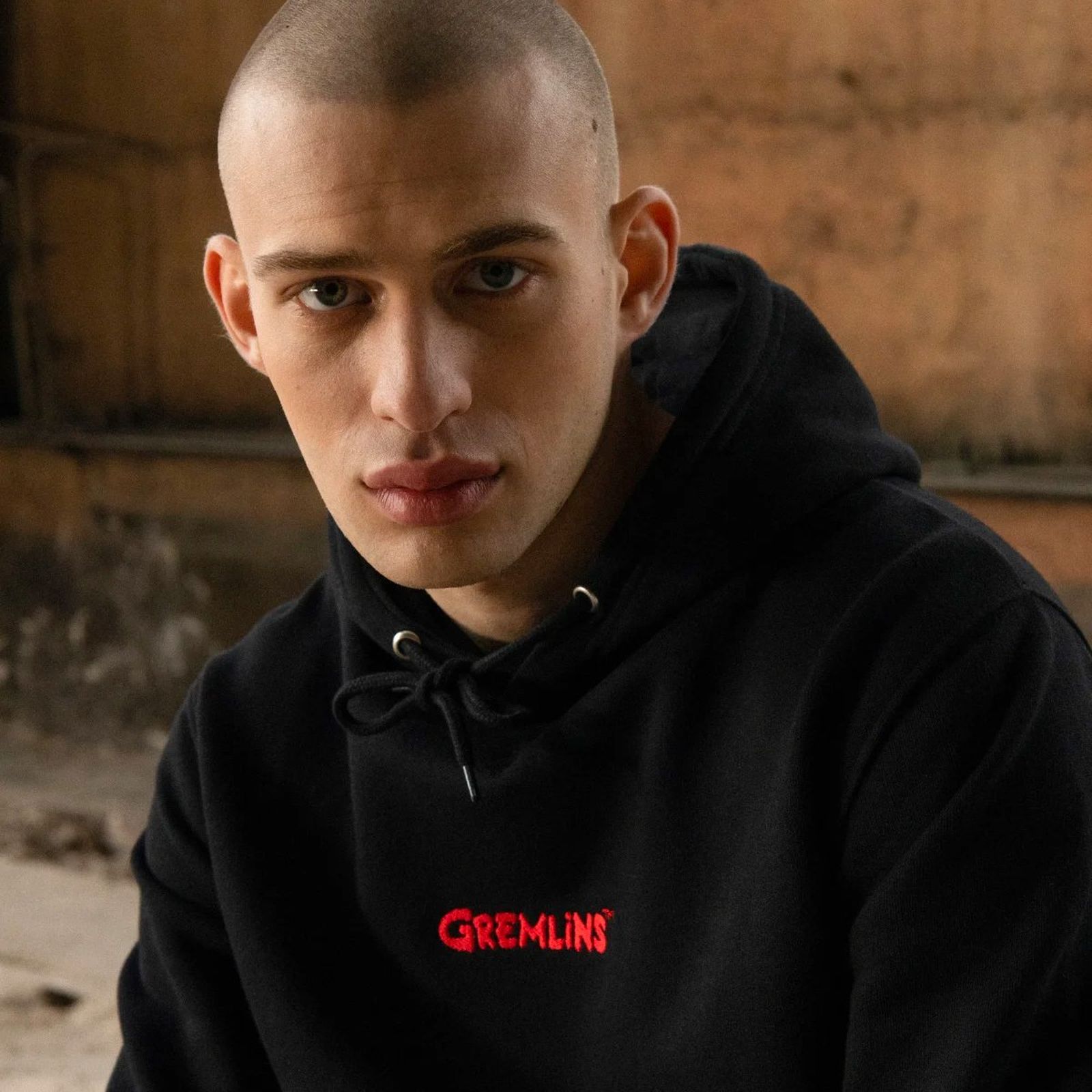 Person in a black hoodie with "Gremlins" written on it, sitting in a dimly lit room with a neutral expression.