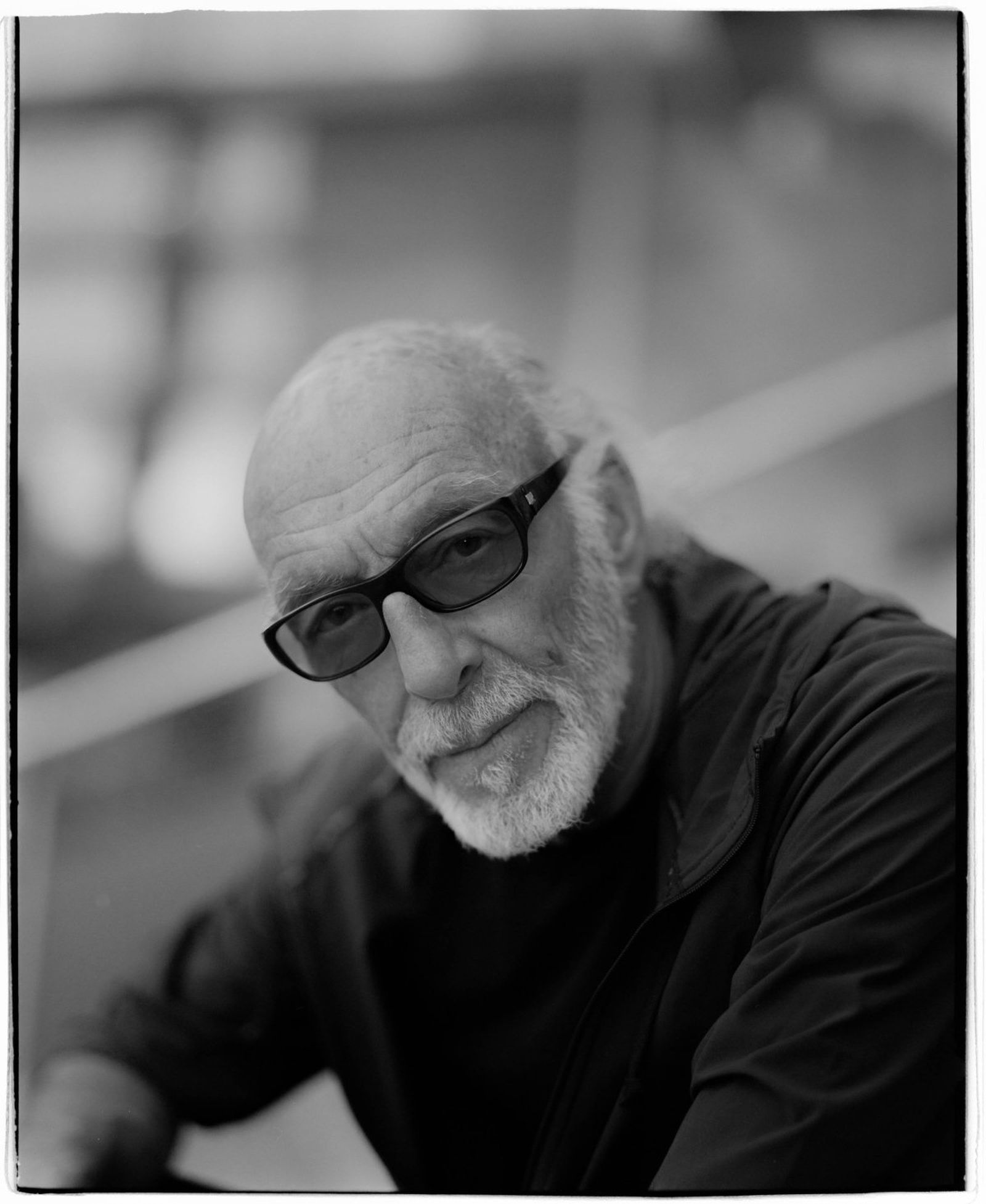Black and white portrait of an older man with glasses, a beard, and a serious expression, wearing a dark jacket.