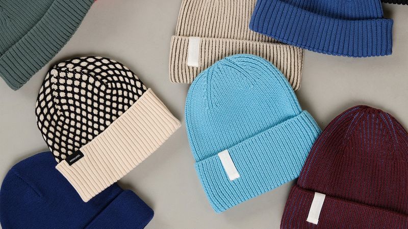 A collection of colorful beanies arranged on a gray surface, featuring various patterns and textures, including blue, beige, and patterned designs.