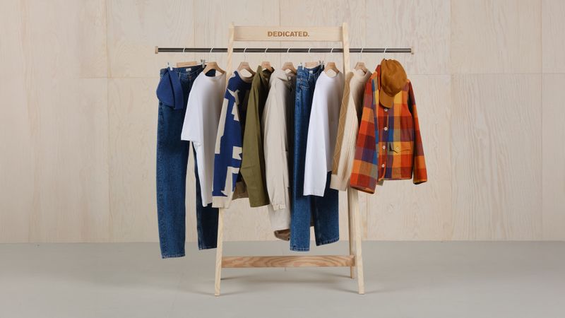 Clothing rack with assorted casual wear, including shirts, jackets, and jeans, displayed against a light wooden background.