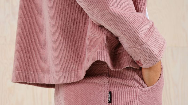 Person wearing a pink corduroy outfit with hands in pockets, showcasing a textured fabric and buttoned sleeve detail.