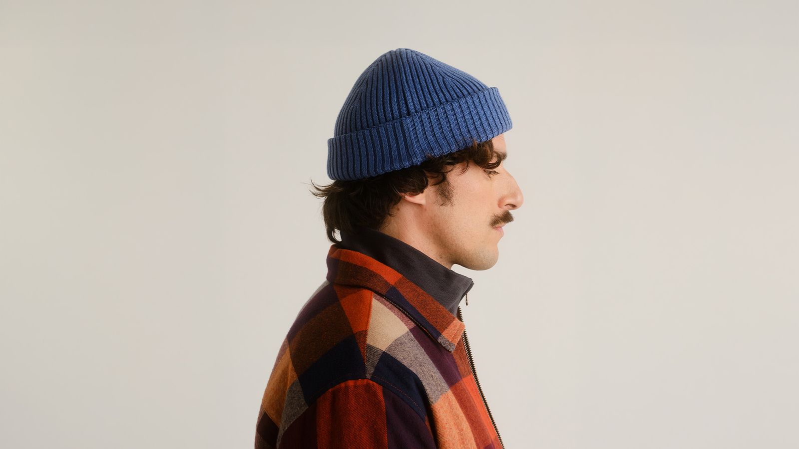 Profile of a person in a blue beanie and plaid jacket, facing left against a plain background.