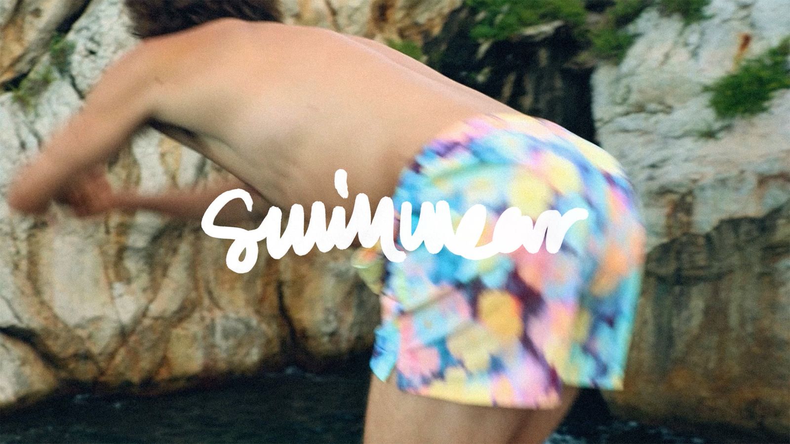 Person diving near cliffs, wearing colorful swim trunks. "Swimwear" text overlays the image.