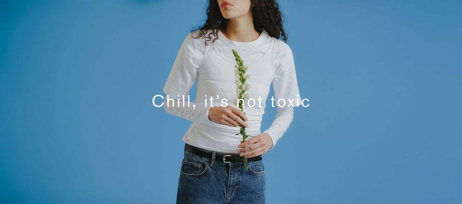 Person in a white shirt holds a green flower against a blue background. Text overlay: "Chill, it's not toxic."