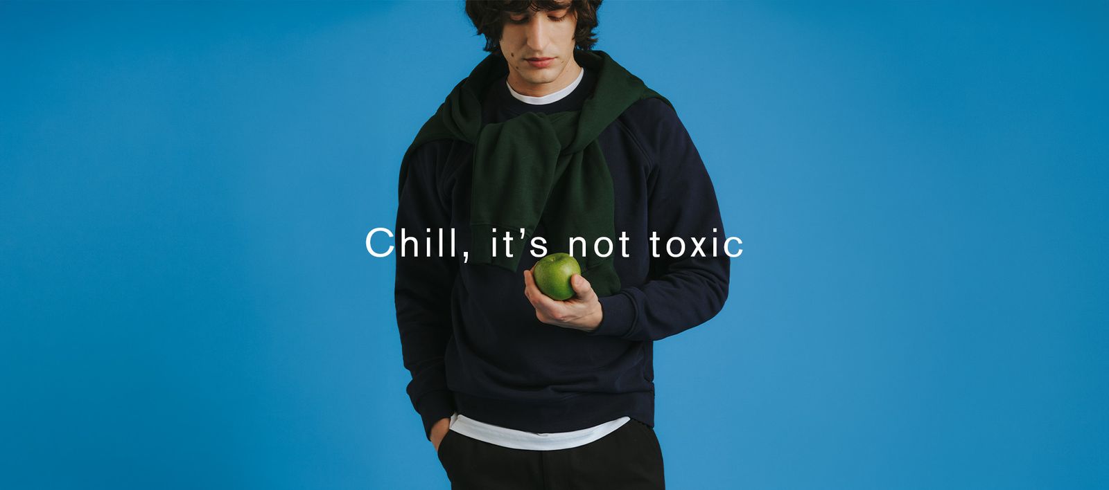 Man in navy sweater holding a green apple, with text "Chill, it’s not toxic" on a blue background.