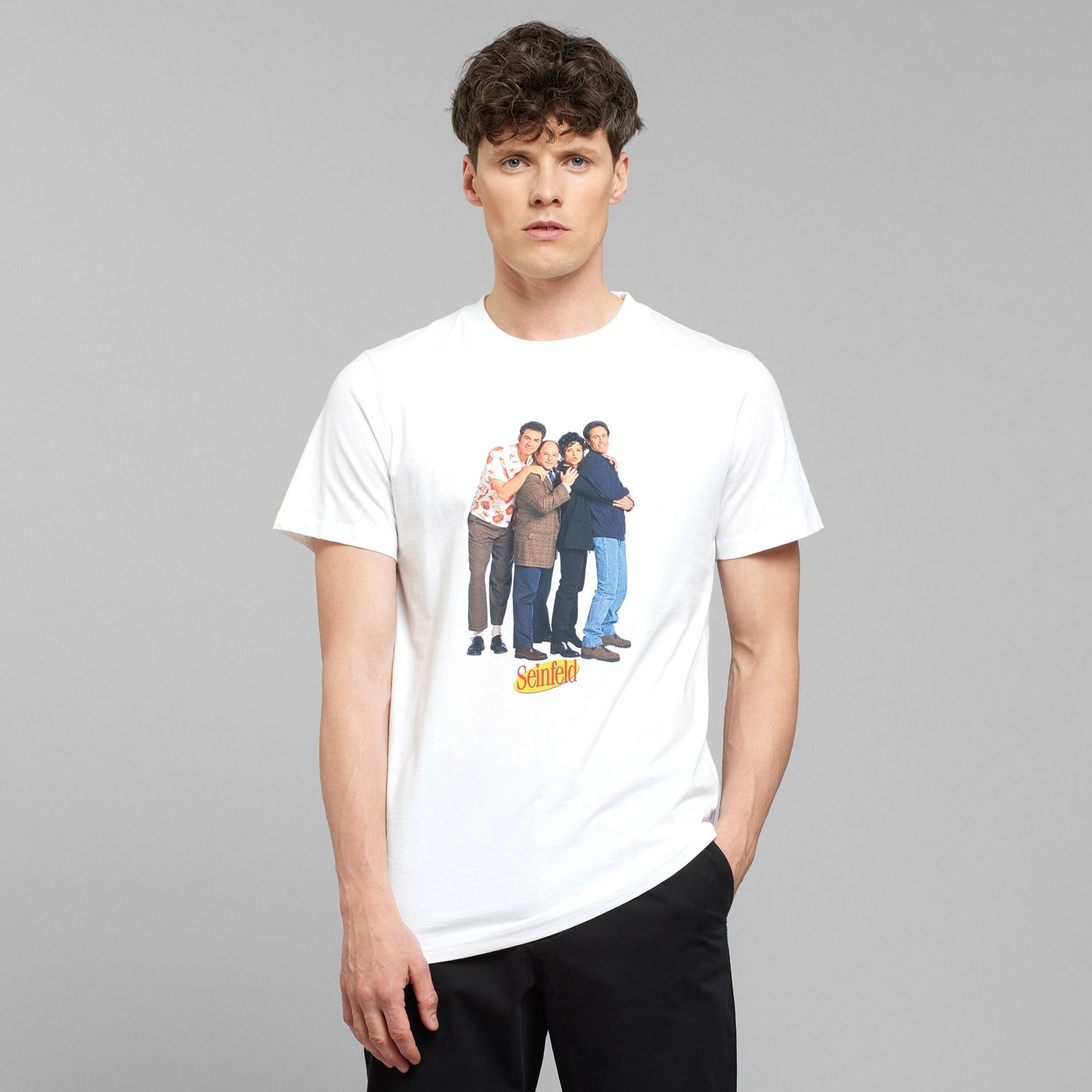 Person wearing a white T-shirt with a group image and "Seinfeld" logo, standing against a plain gray background.