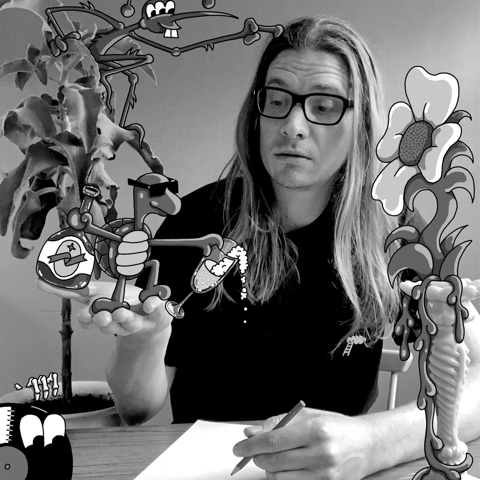 Man with long hair and glasses drawing at a table, surrounded by whimsical, cartoon-like creatures and plants in black and white.