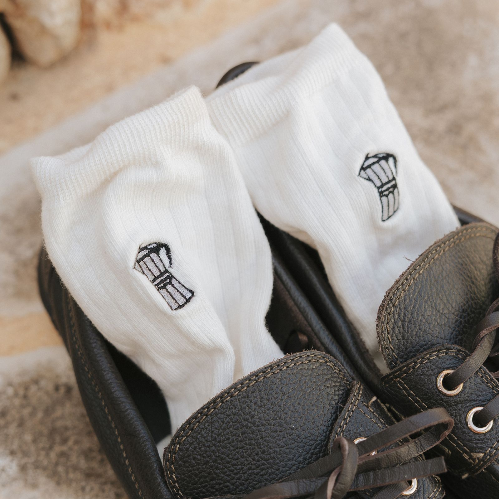 White socks with a coffee pot design tucked into black leather shoes on a stone surface.
