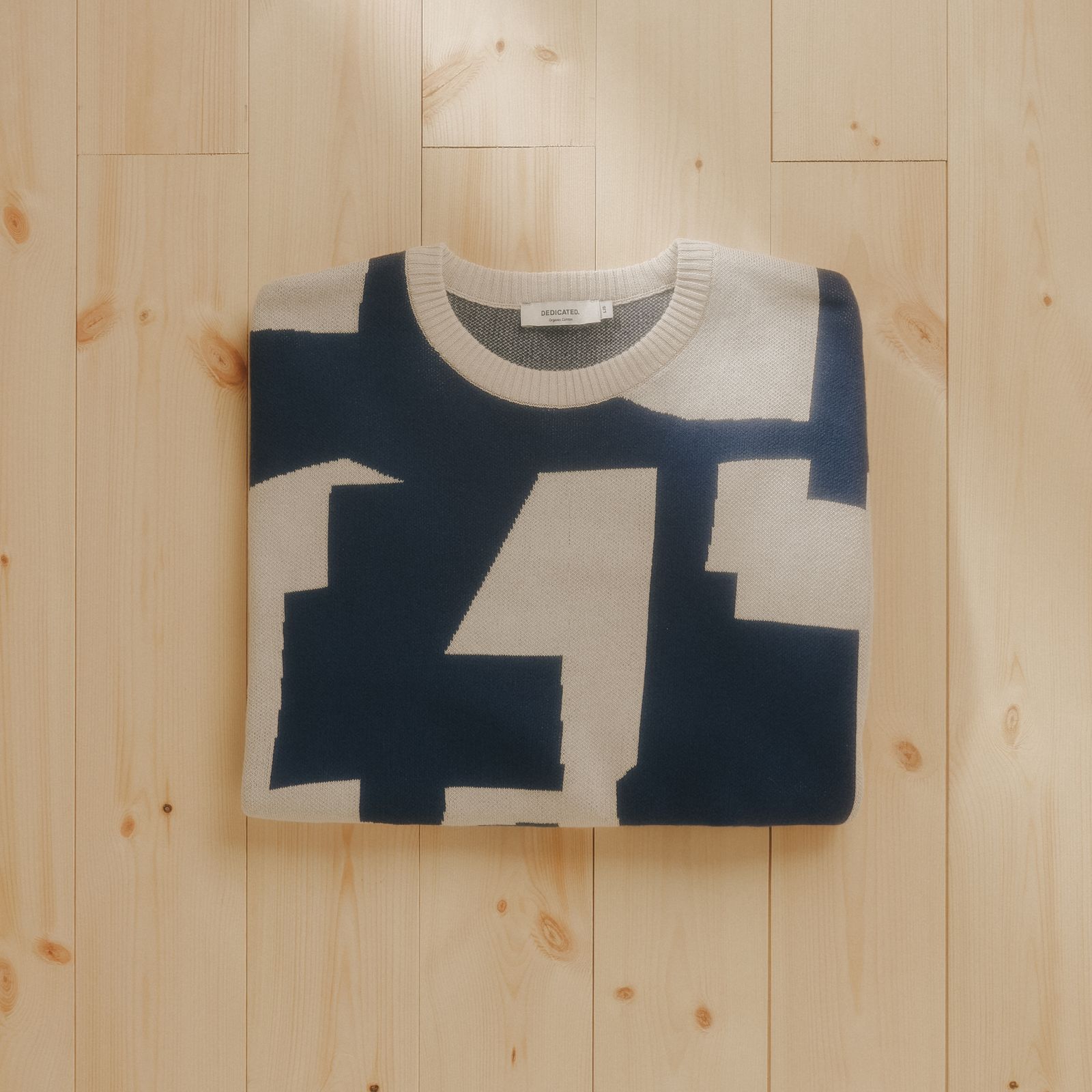 A folded sweater with a bold, abstract navy and white pattern, placed on a light wooden floor.