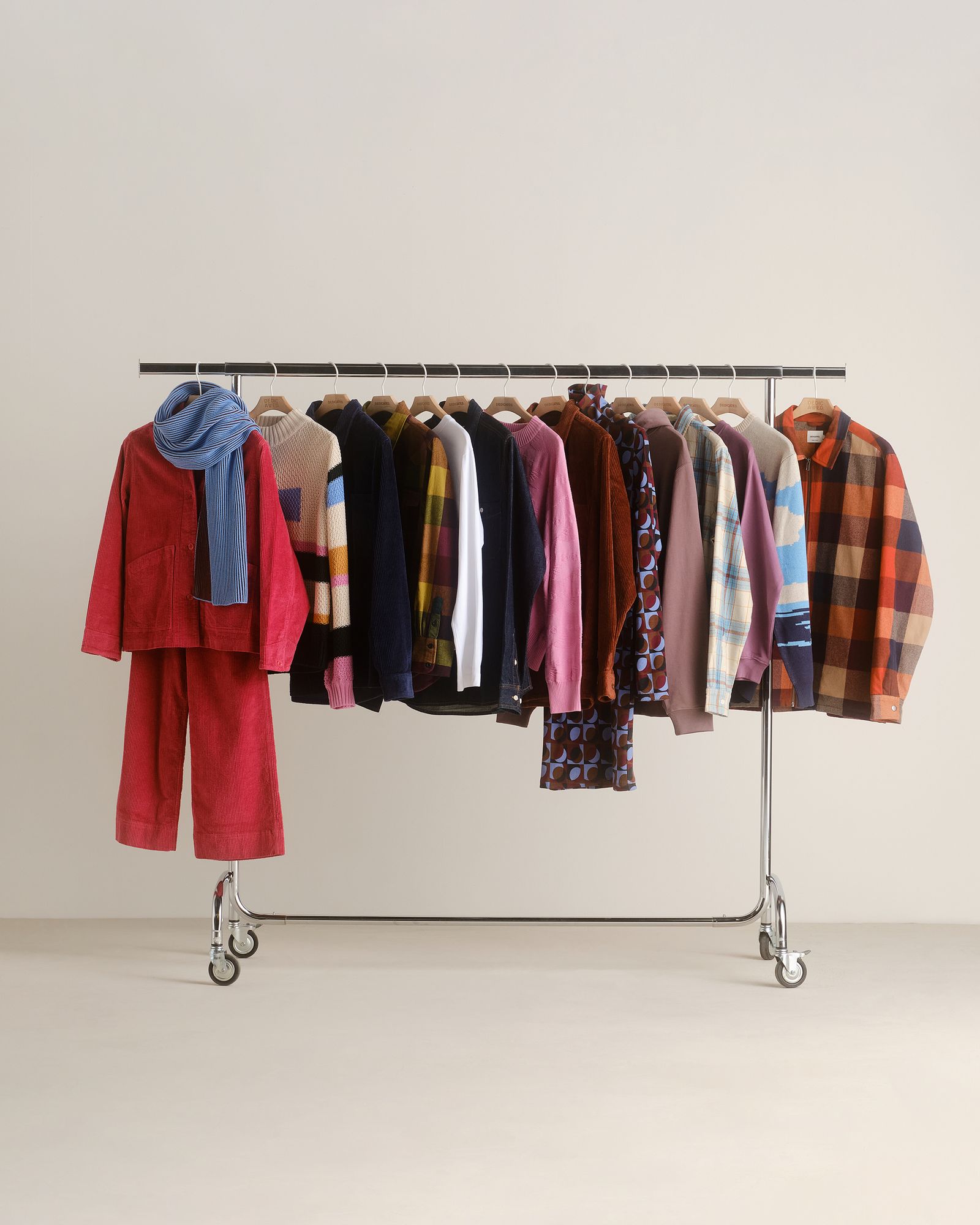 A clothing rack with various colorful garments including sweaters, jackets, and coats, featuring a blue scarf draped over a red outfit.