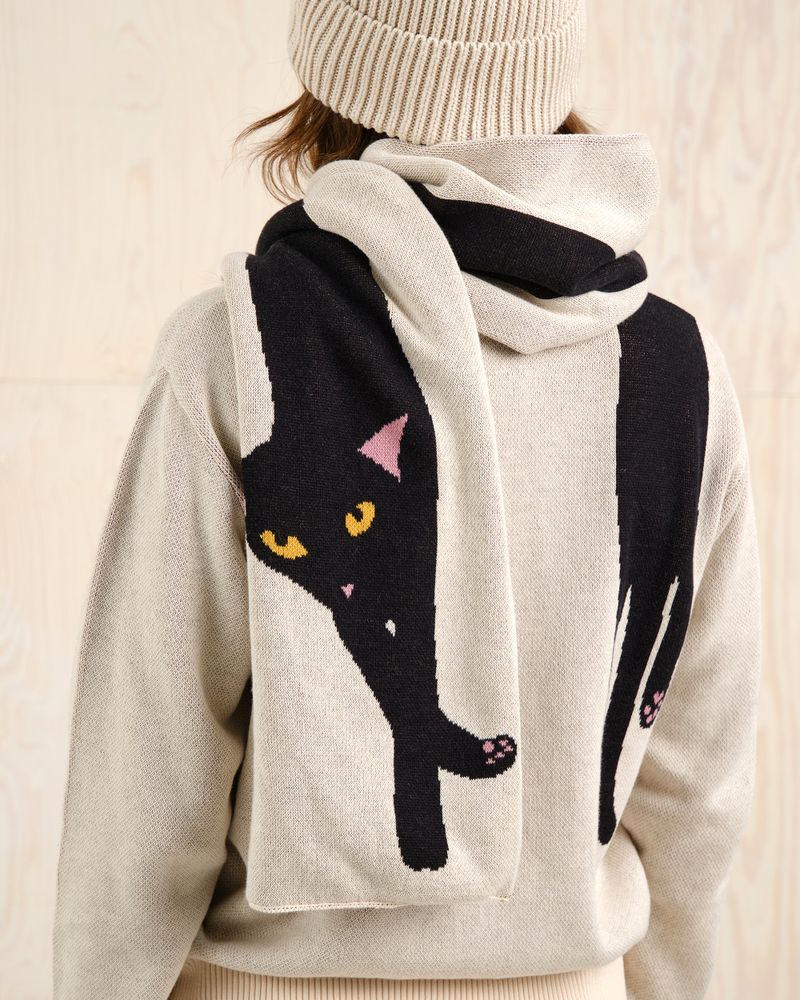Person wearing a beige outfit with a matching scarf featuring a black cat design.