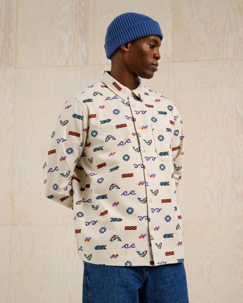 Person wearing a patterned shirt with geometric designs and a blue knit hat, standing against a light wooden background.