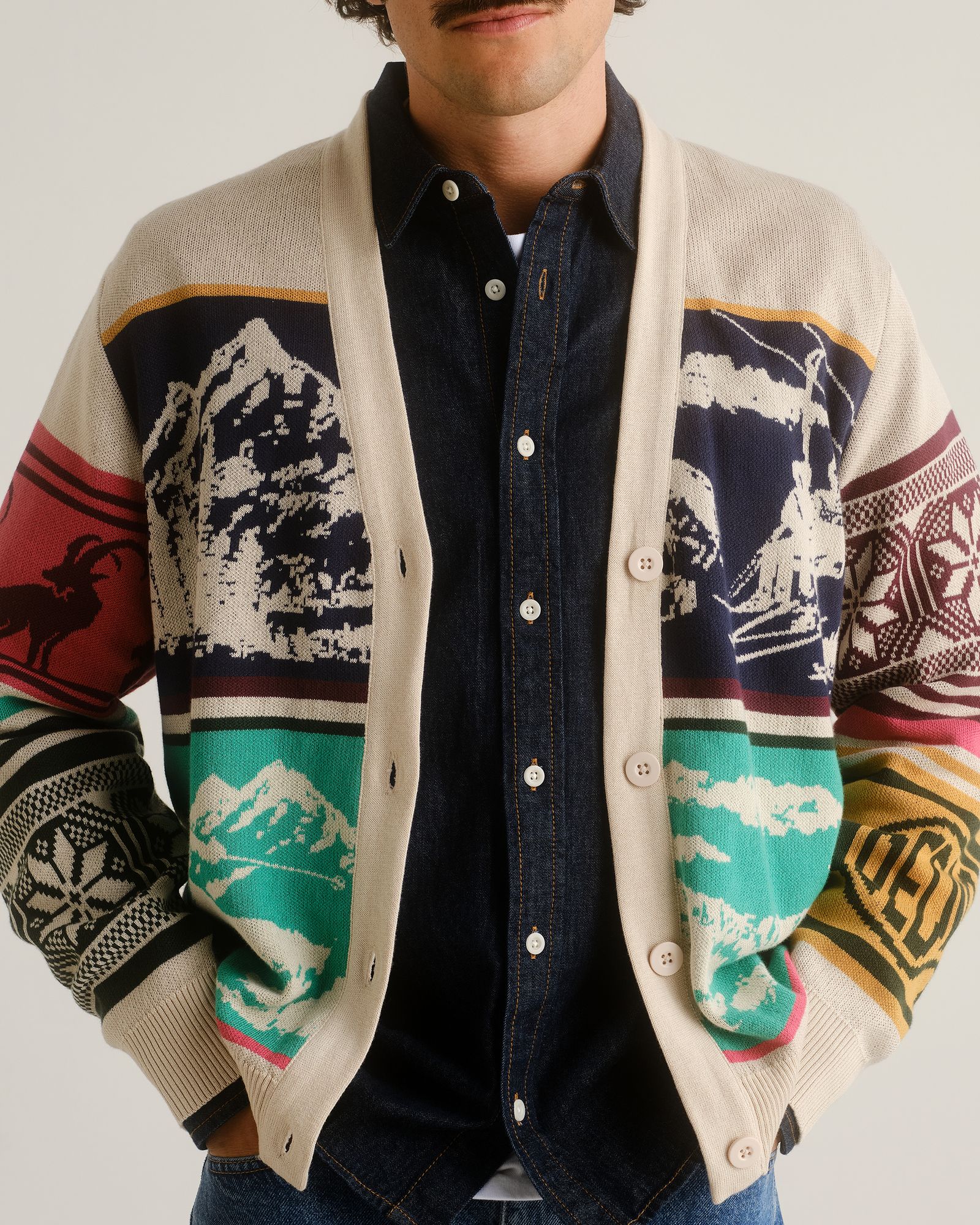 A person wearing a colorful patterned cardigan over a dark denim shirt, partially visible from the chest down.
