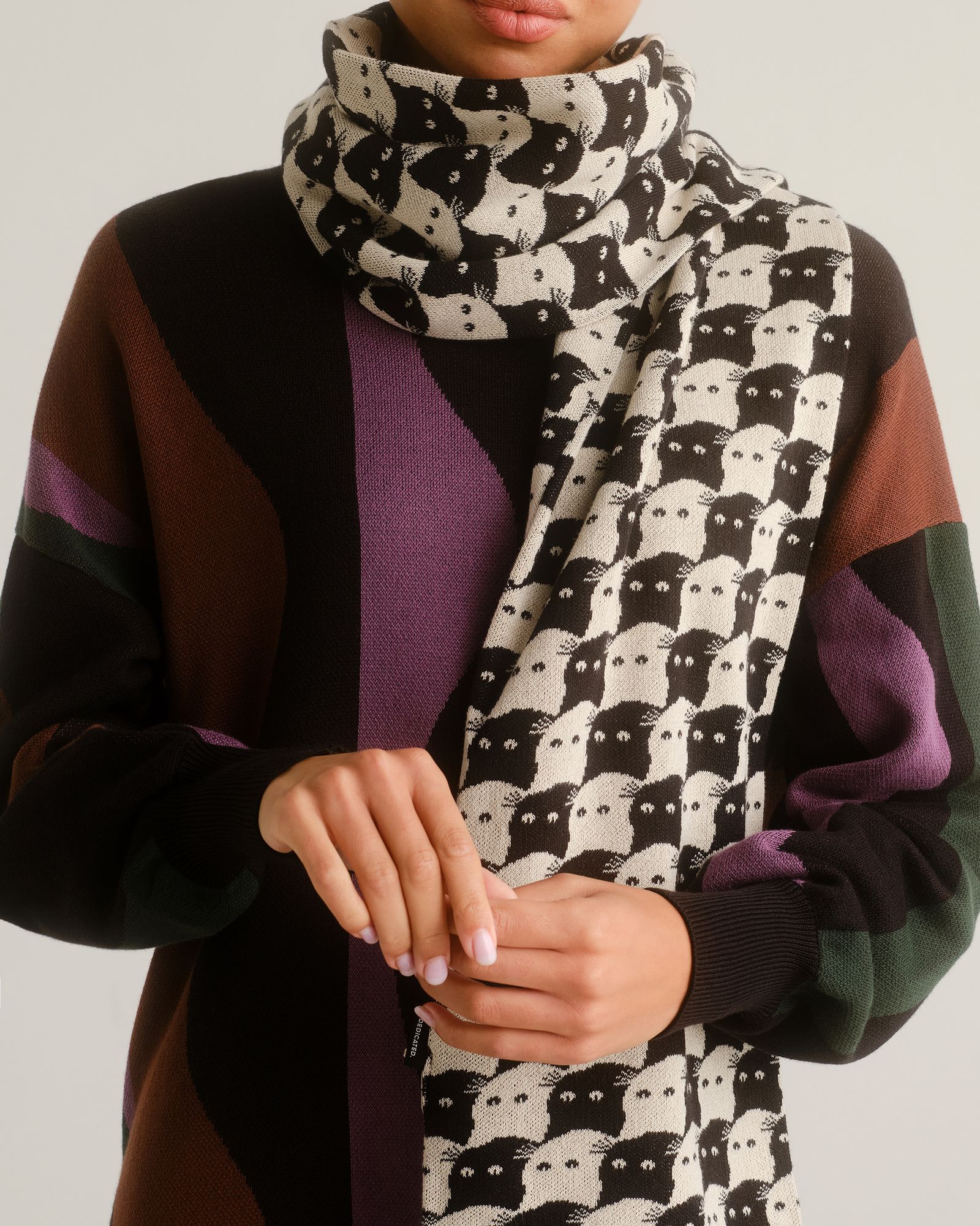 Person wearing a patterned scarf with white and black cat faces, paired with a colorful sweater with abstract shapes.