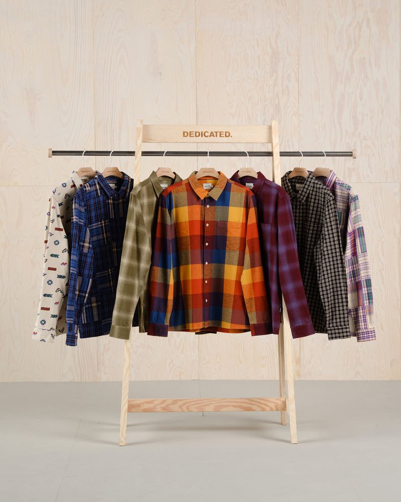 A wooden rack displays a variety of colorful plaid and patterned shirts, neatly hung on hangers against a light wood background.
