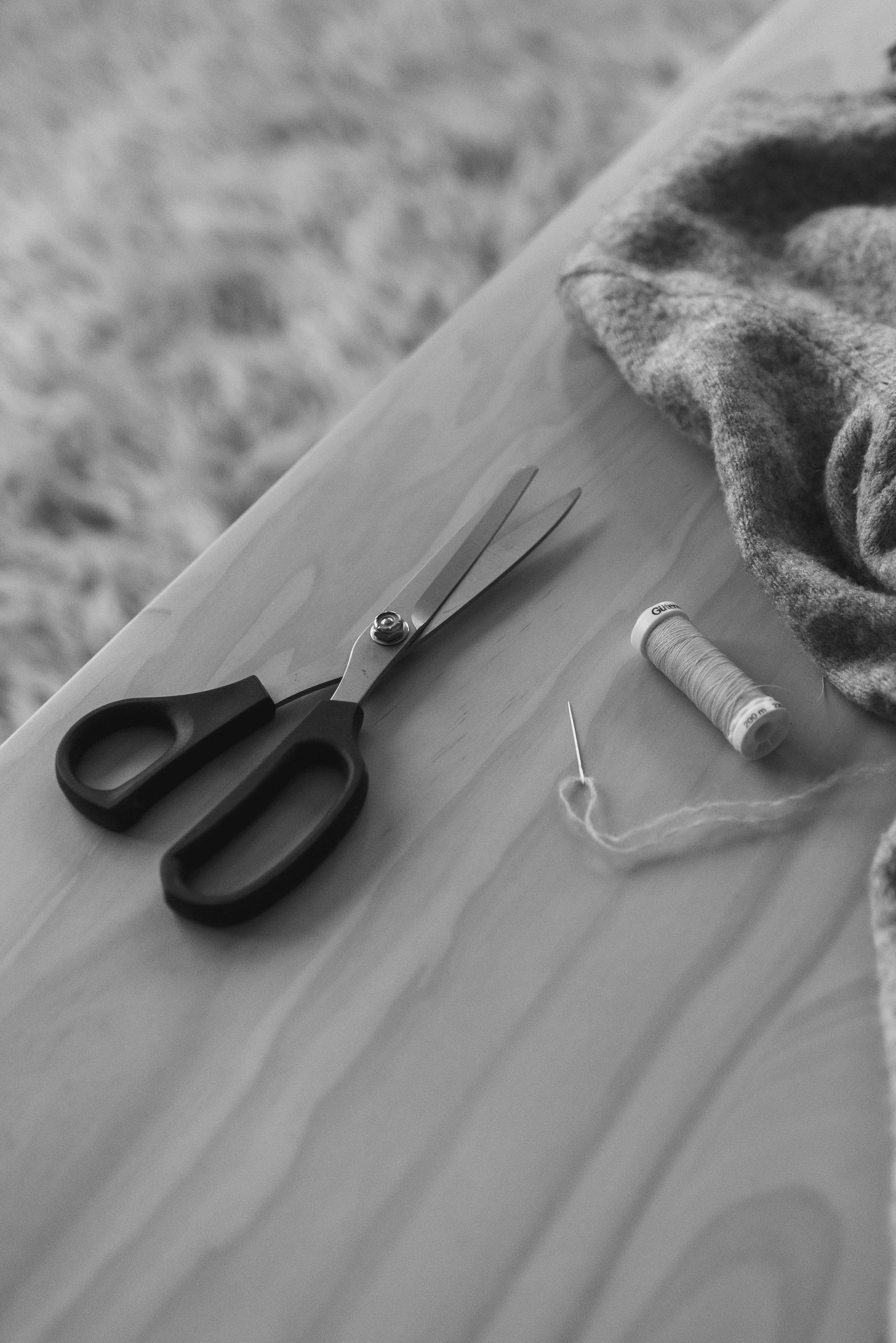 black and white a sweater on a table with scissors and a thread roll
