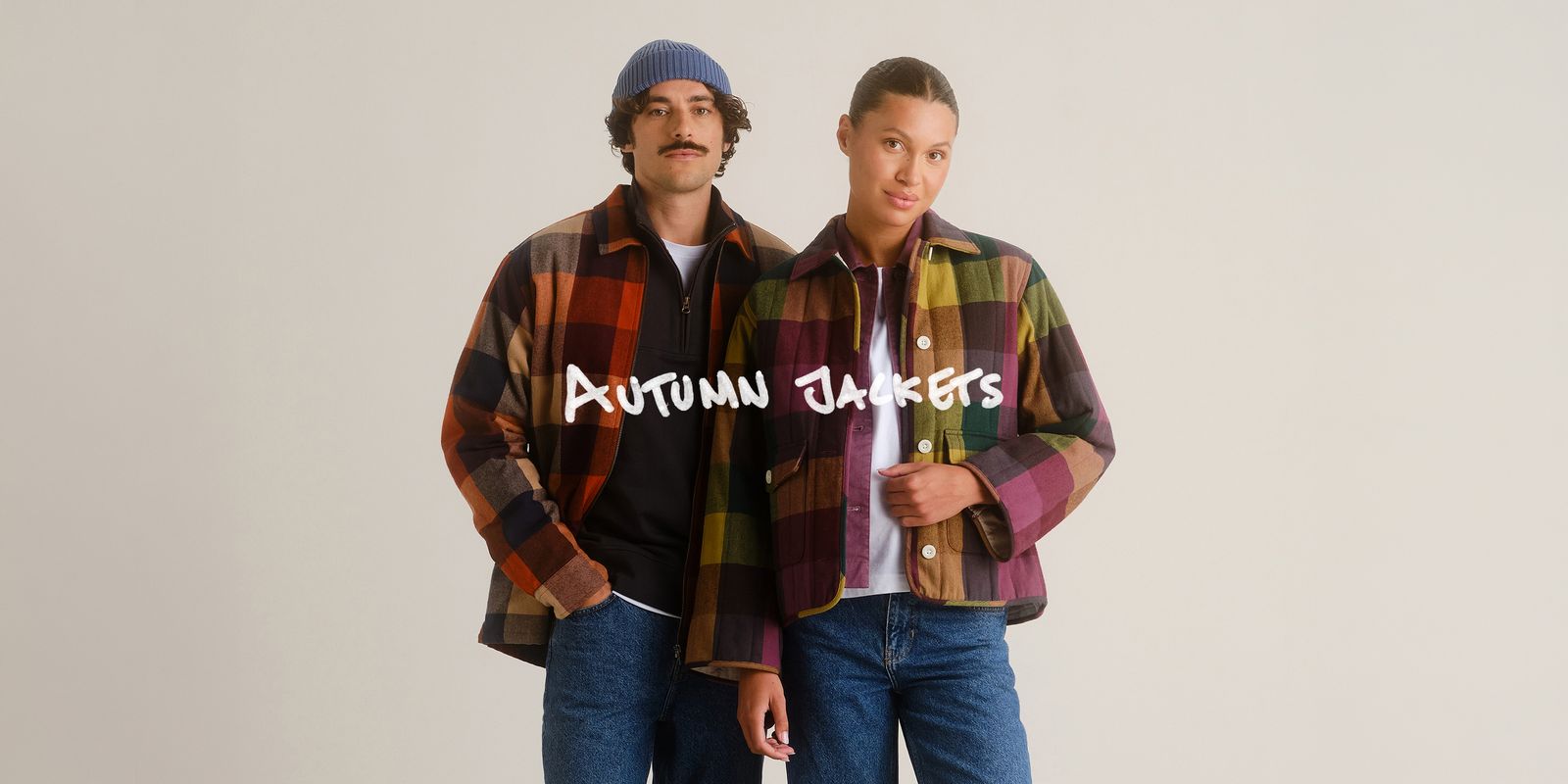 Two people wearing colorful plaid jackets, one in a beanie, both in jeans, standing against a neutral background. Text reads "Autumn Jackets."