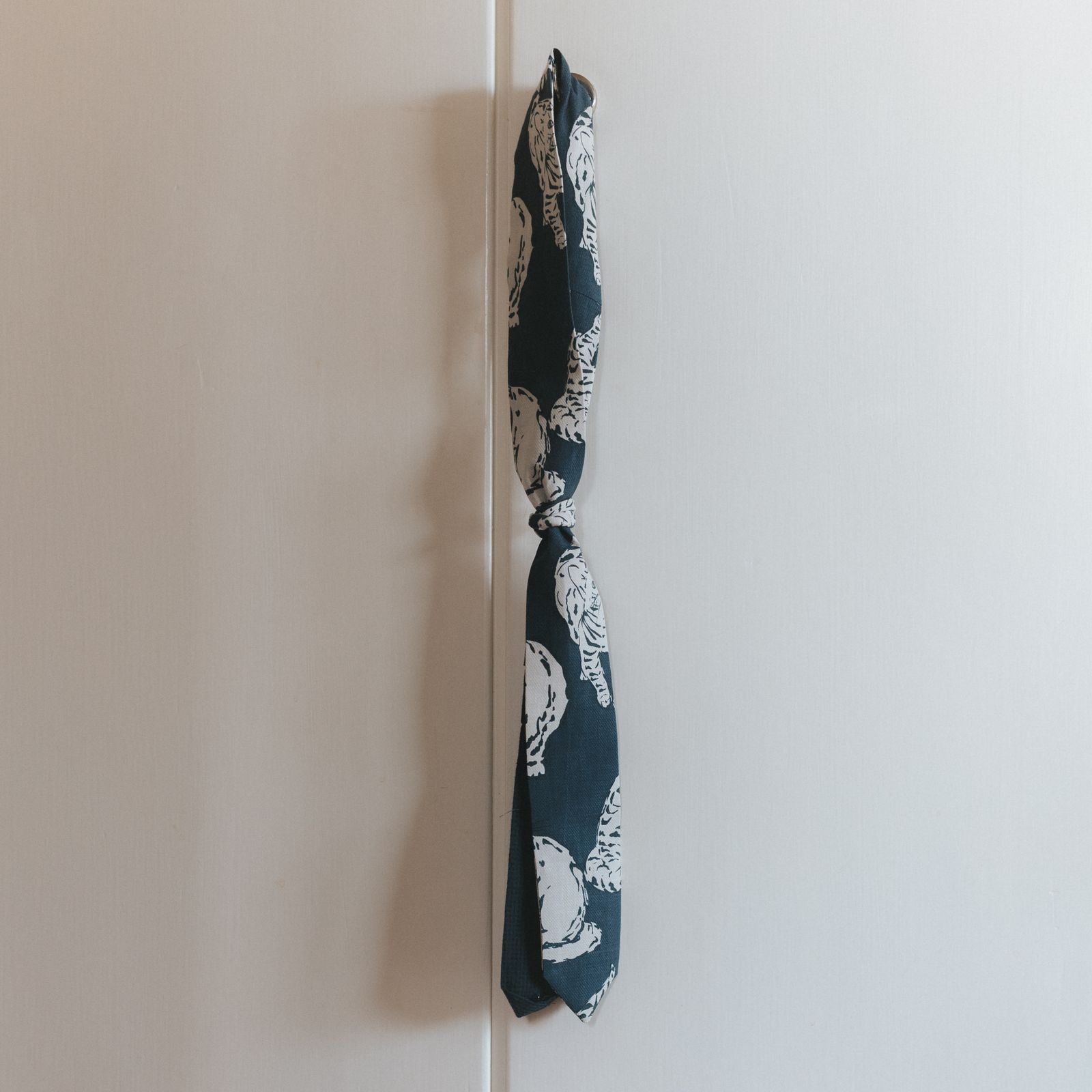 A tie made of a white and blue printed fabric, hanging on a door