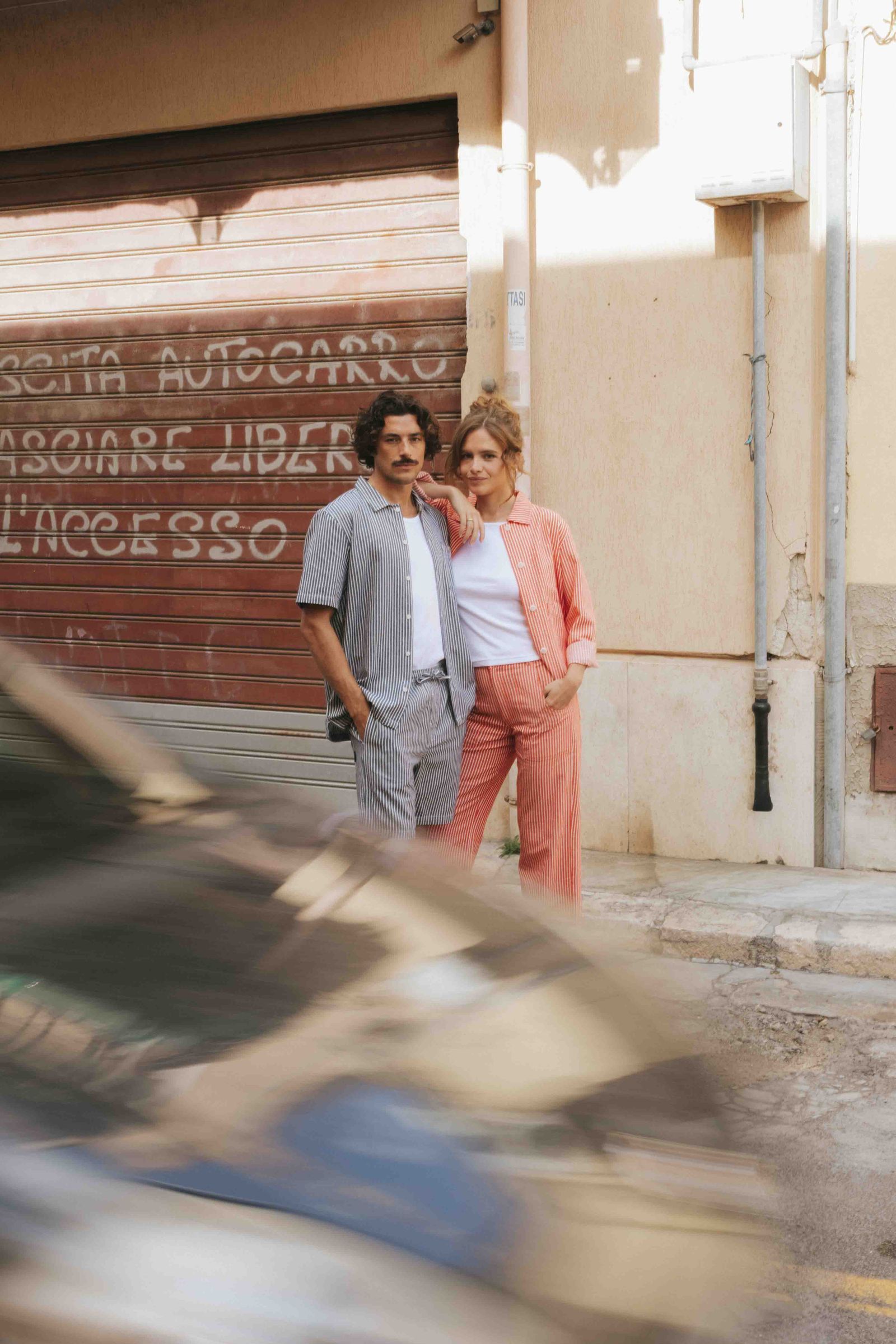A guy and a woman standing infront of a garage, with a car passing by