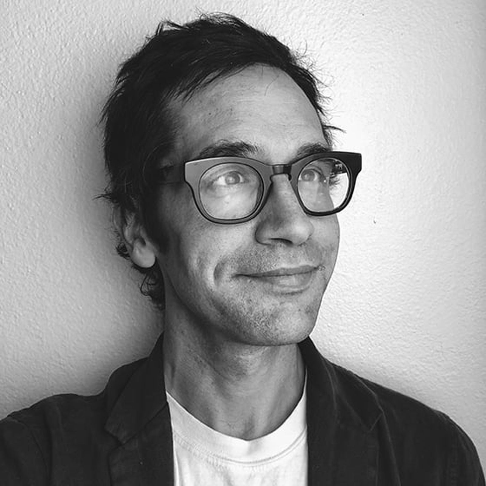 Black and white photo of a person with glasses, short hair, and a slight smile, looking to the side against a plain background.