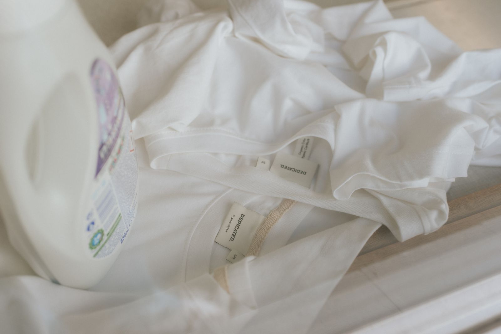 2 white dedicated tshirts with laundry detergent bottle horizontal