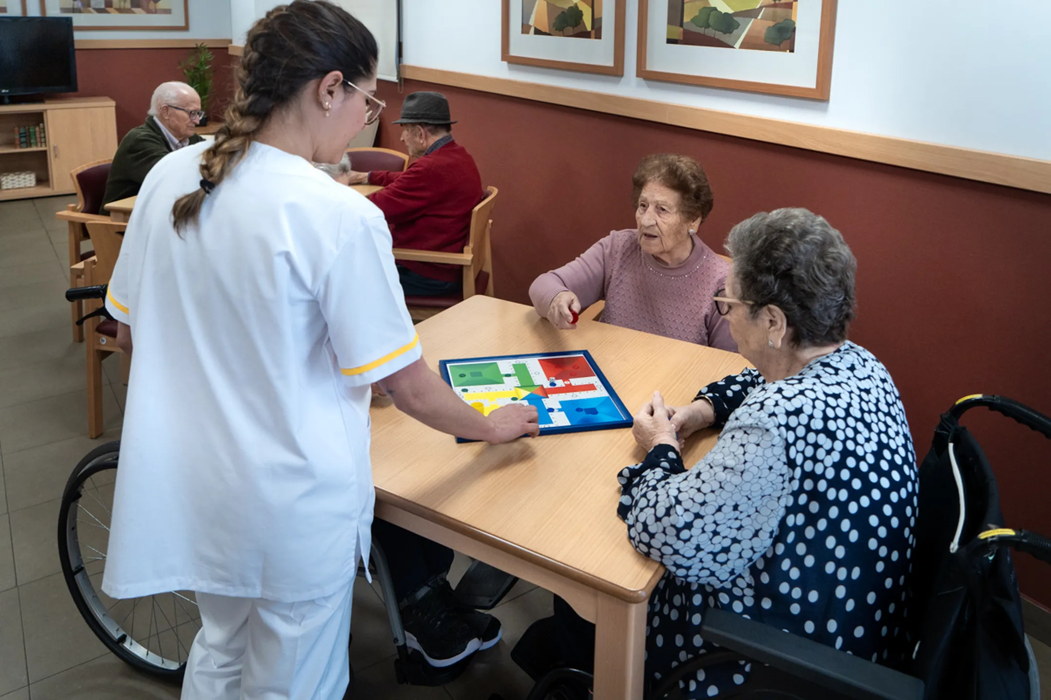 cuidadora y ancianas jugando al parchís