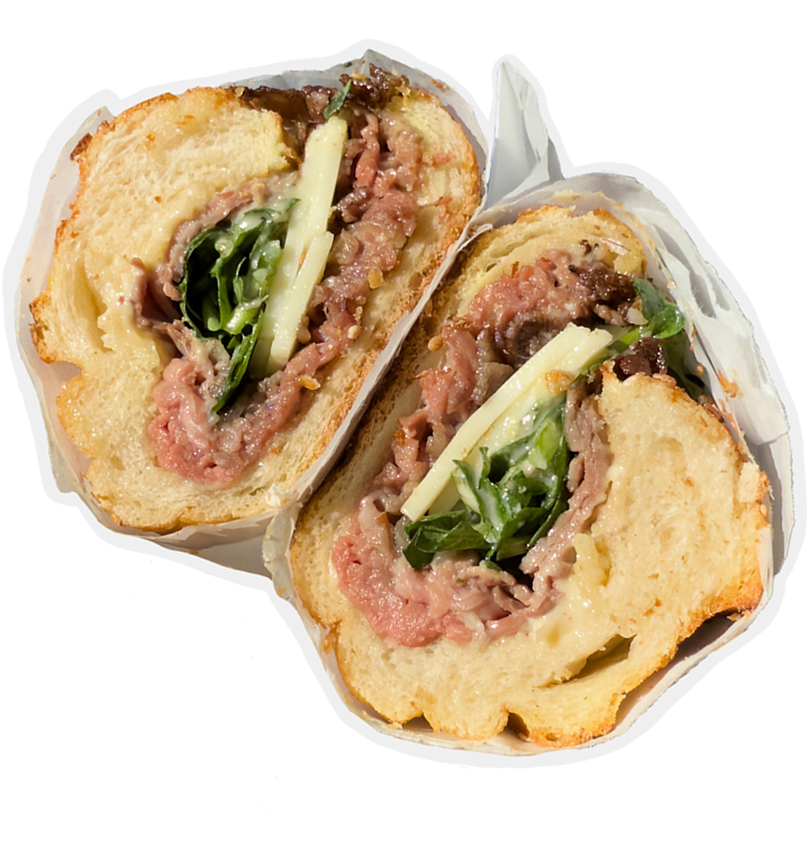 A sandwich cut in half, showing layers of meat, cheese, arugula, and sauce, wrapped in paper on white background.