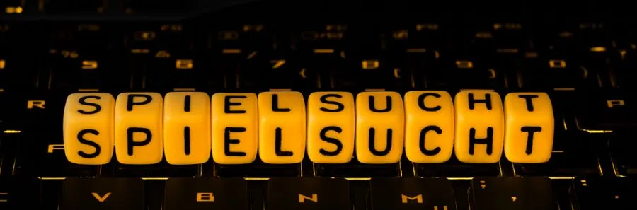 Gelbe Würfel mit dem Wort „Spielsucht“ auf einer Tastatur – Symbol für Online-Glücksspielsucht.