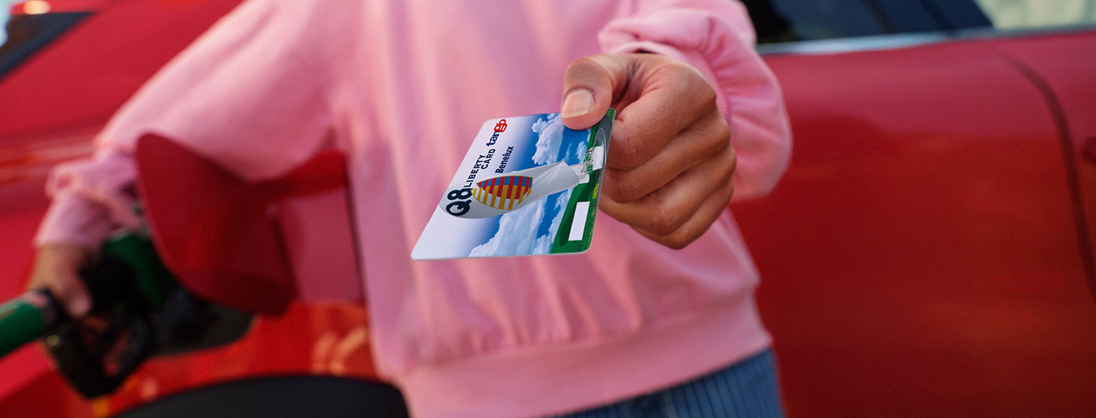 Een hand houdt een Q8 liberty card vast tegen een achtergrond van een drukke stadssnelweg met fileverkeer in de schemering.